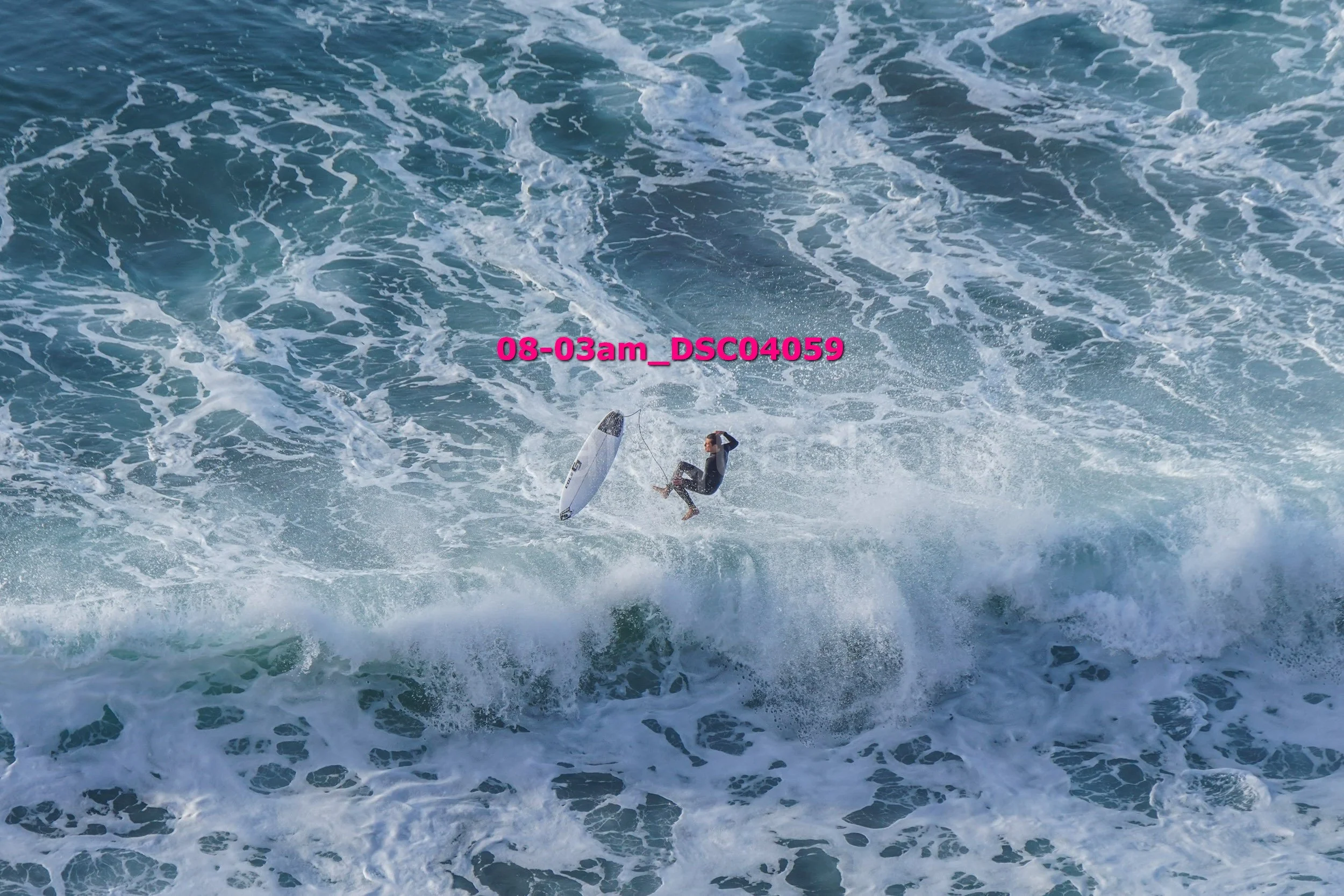 A person surfing on a large wave in the ocean, with a surfboard in mid-air and water splashing around.