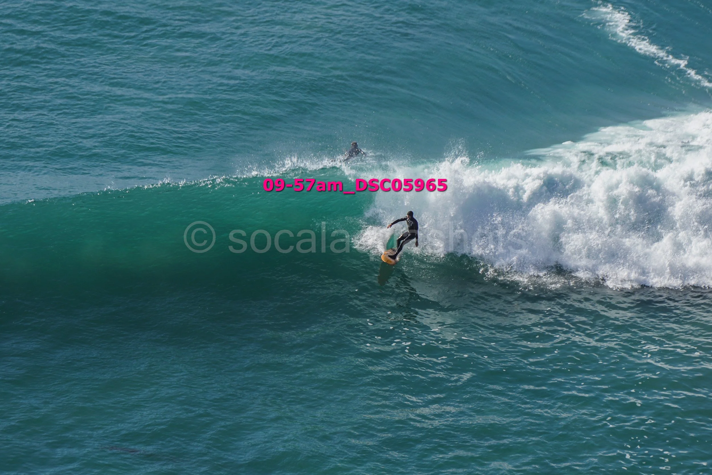 A surfer riding a wave in the ocean, with another surfer visible in the background.