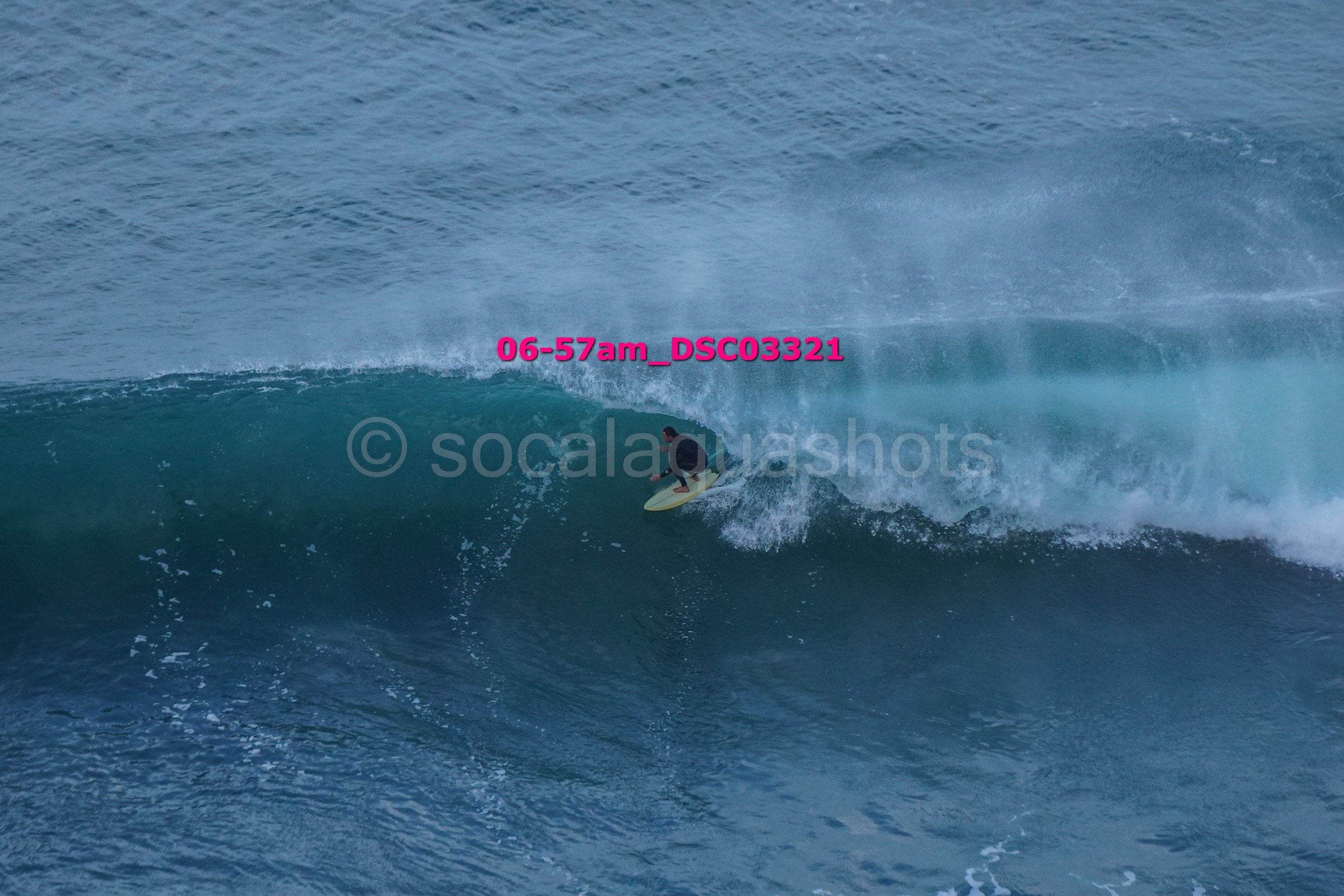 A person surfing on a large wave in the ocean, with a visible watermark and pink text overlay.