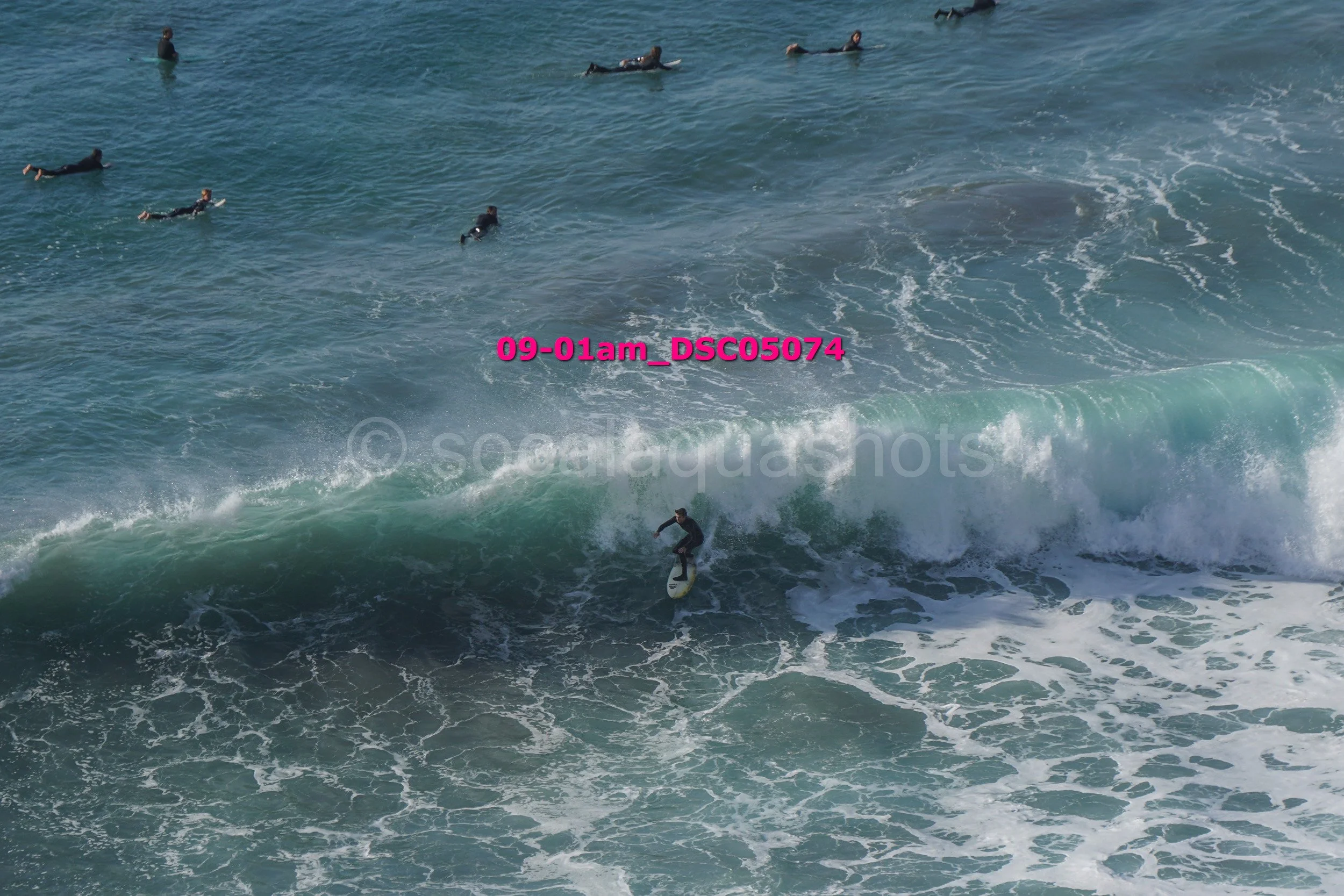 A surfer riding a wave with several people swimming and floating in the water nearby.