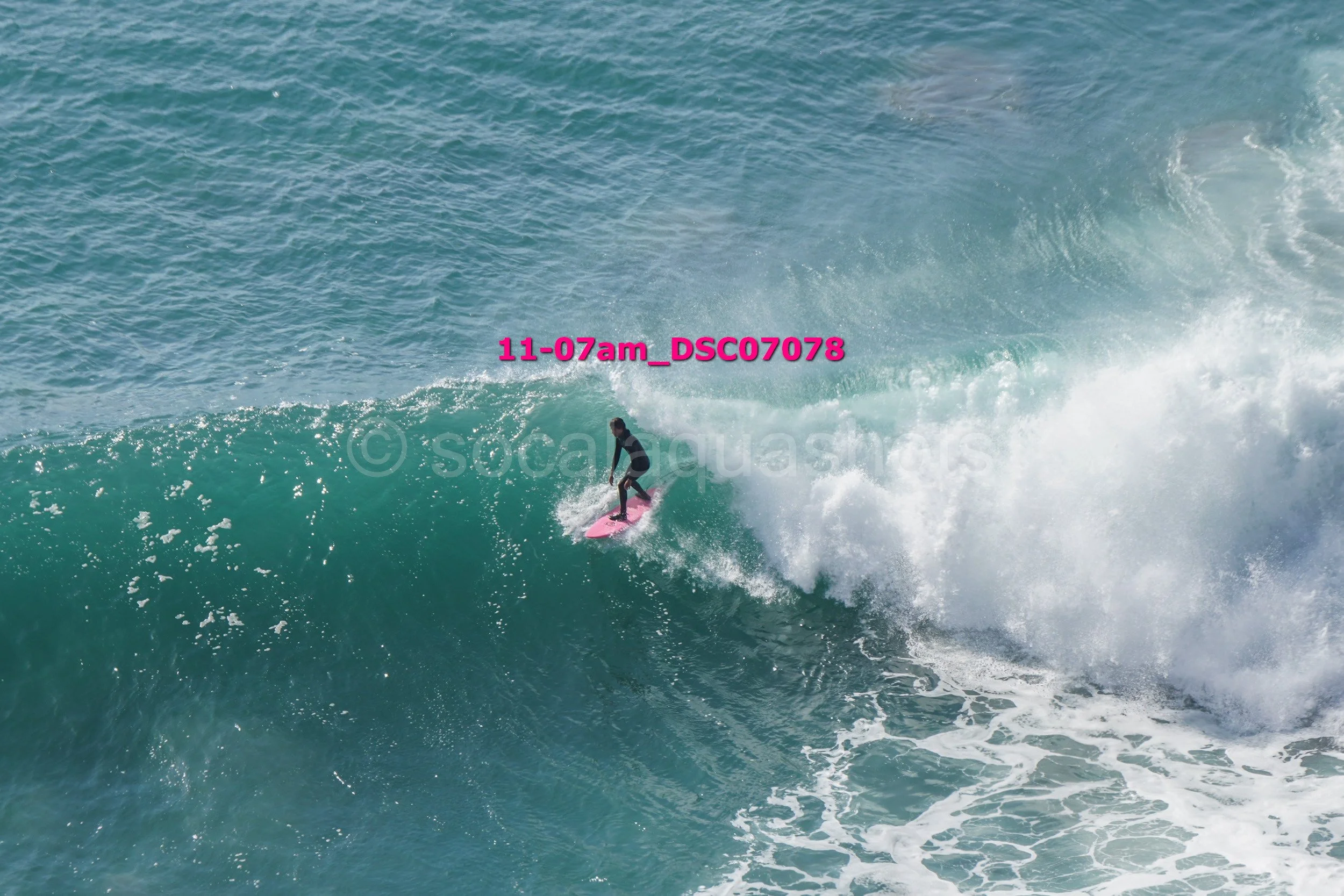 A person surfing on a pink surfboard riding a large wave in the ocean.