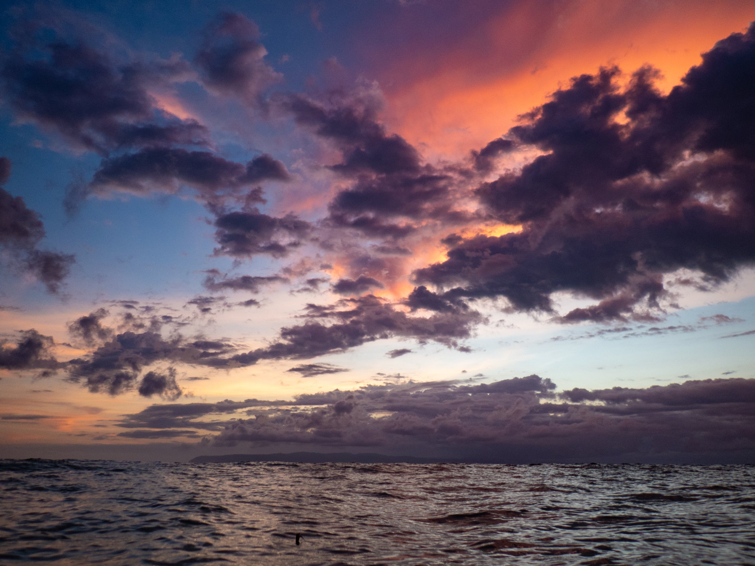 A colorful sunset over a body of water with dark clouds in the sky.