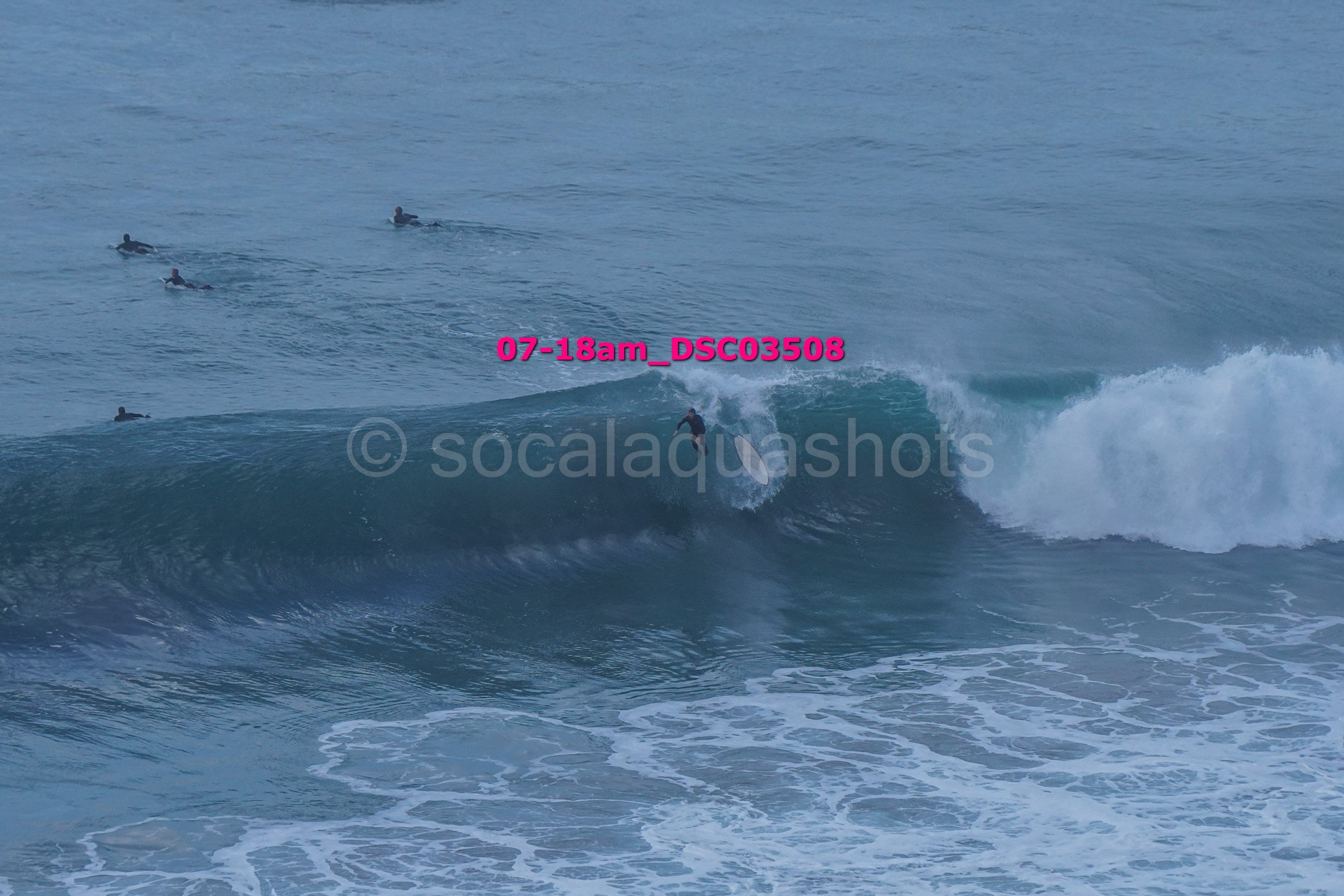 A person surfing a wave in the ocean with four other surfers watching from a distance.