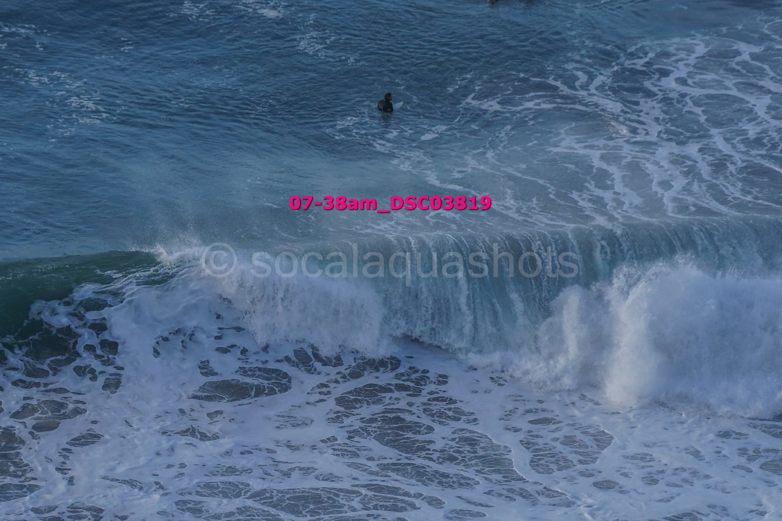 A person surfing in the ocean on a wave, with surfboard, water splashing around.