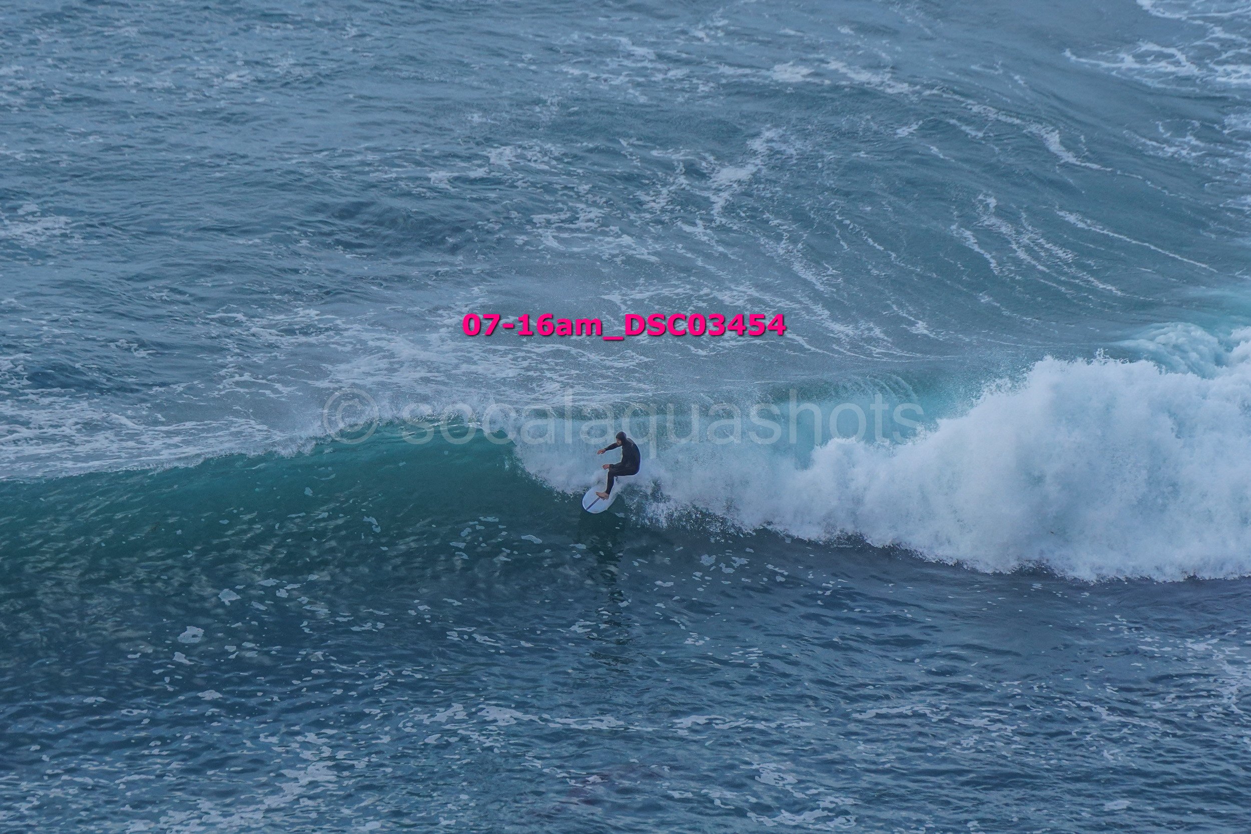 Surfer riding a wave on the ocean with visible water spray and foam.