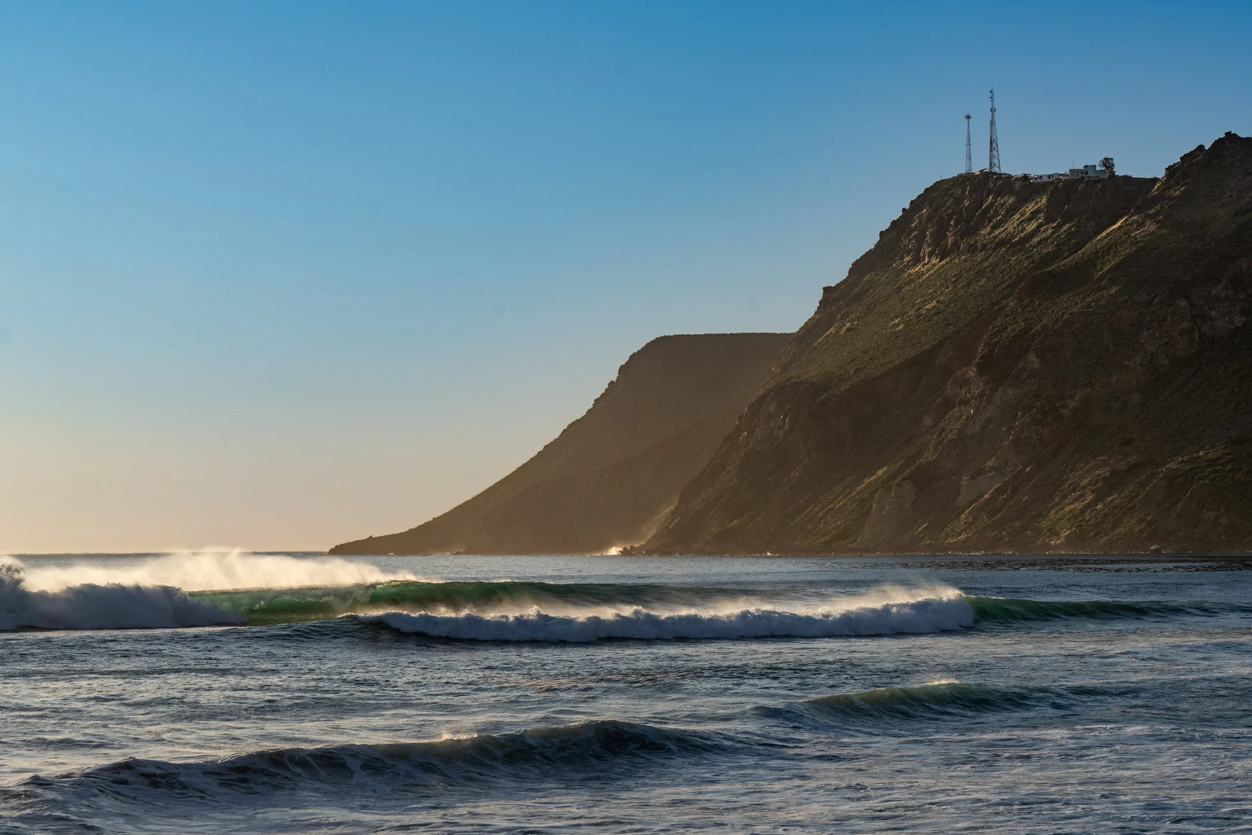 Coastal scene with waves crashing in the ocean and a mountain with communication towers on top