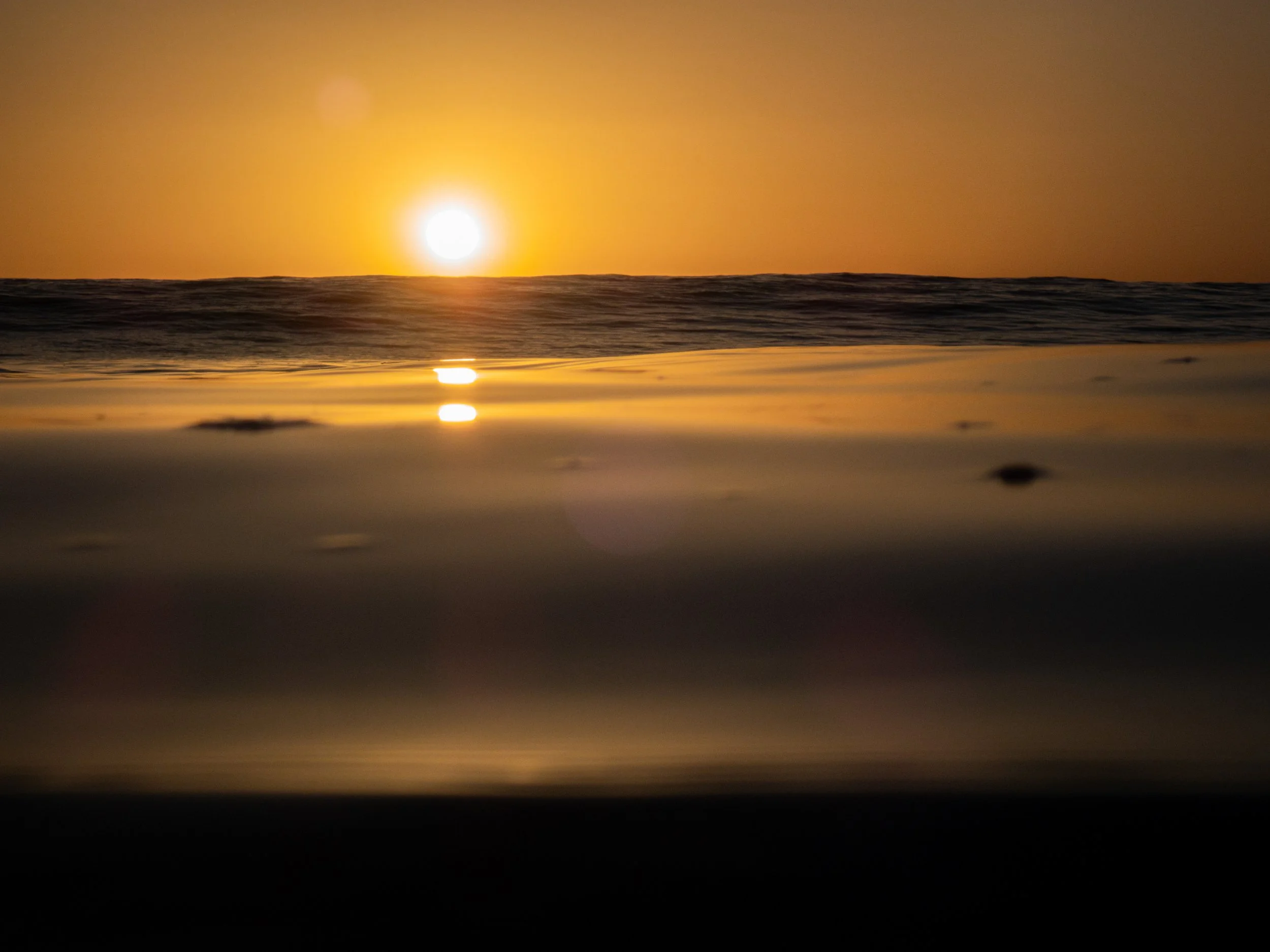 Sunset over the ocean with the sun near the horizon, reflecting on the water's surface.