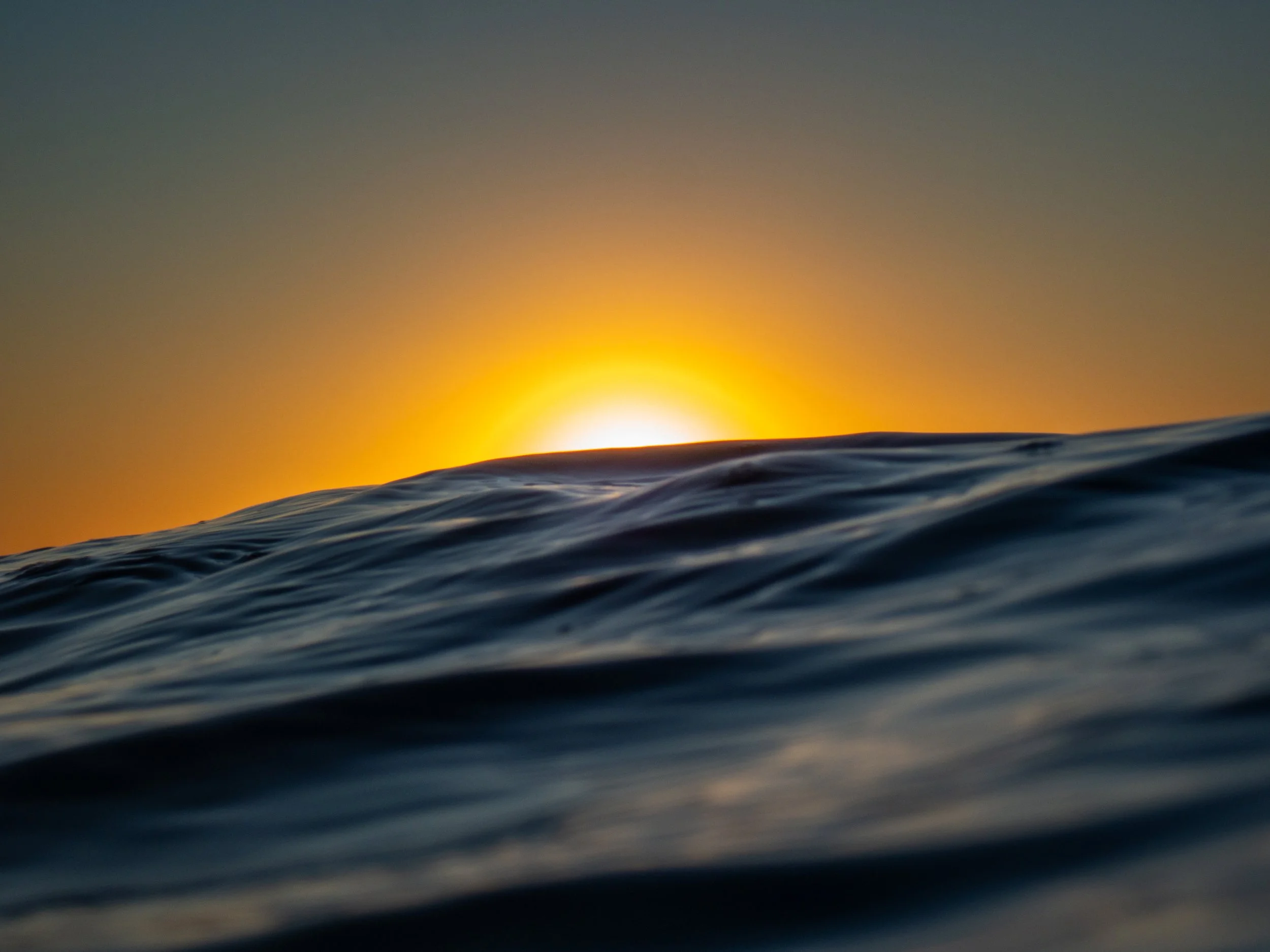 View of ocean waves at sunset with the sun partially visible on the horizon.