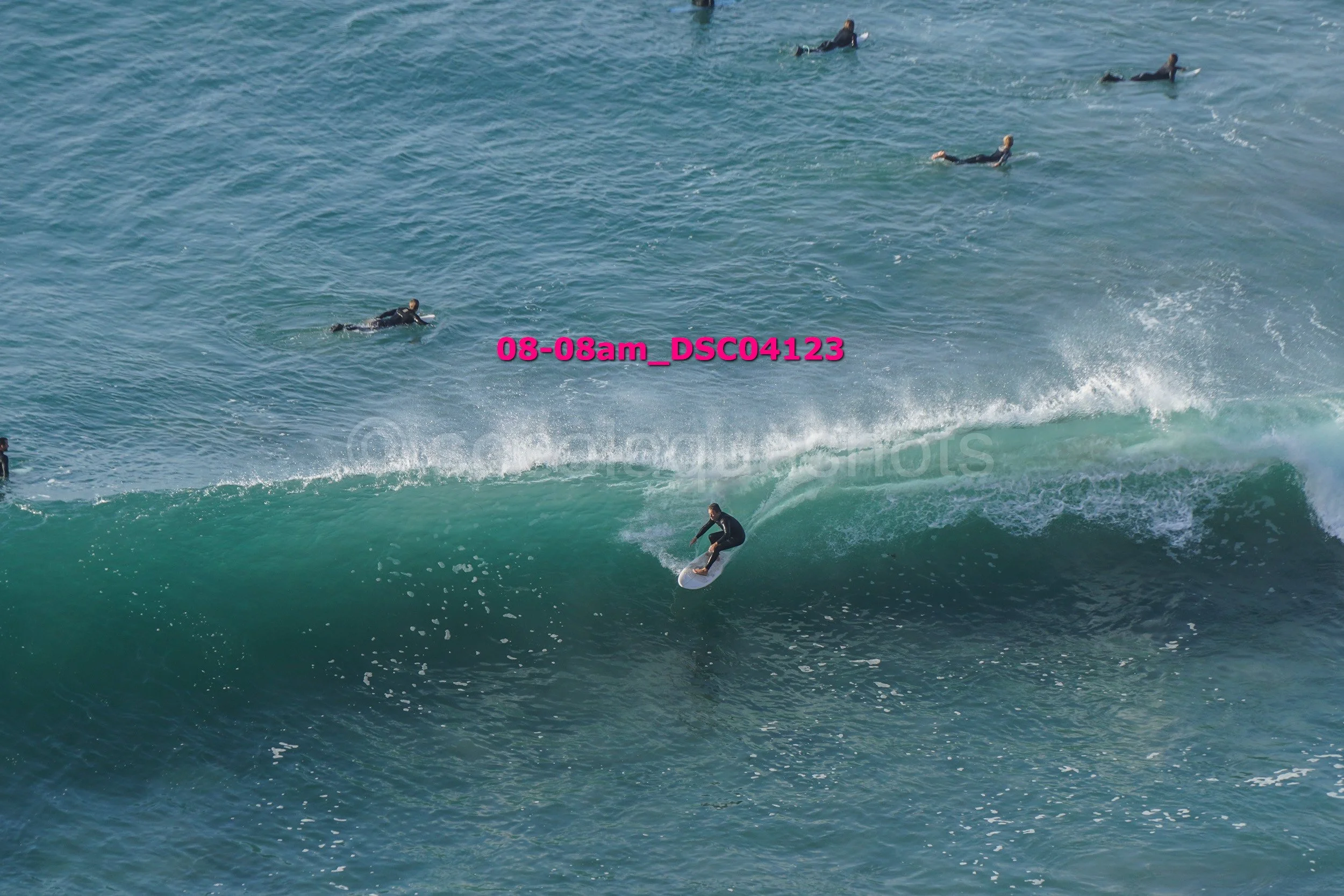 Surfer riding a wave while other surfers wait in the water.