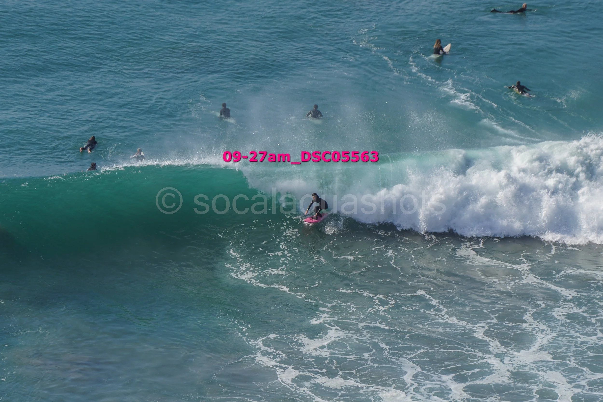 A surfer riding a wave while several surfers paddle in the background in the ocean.