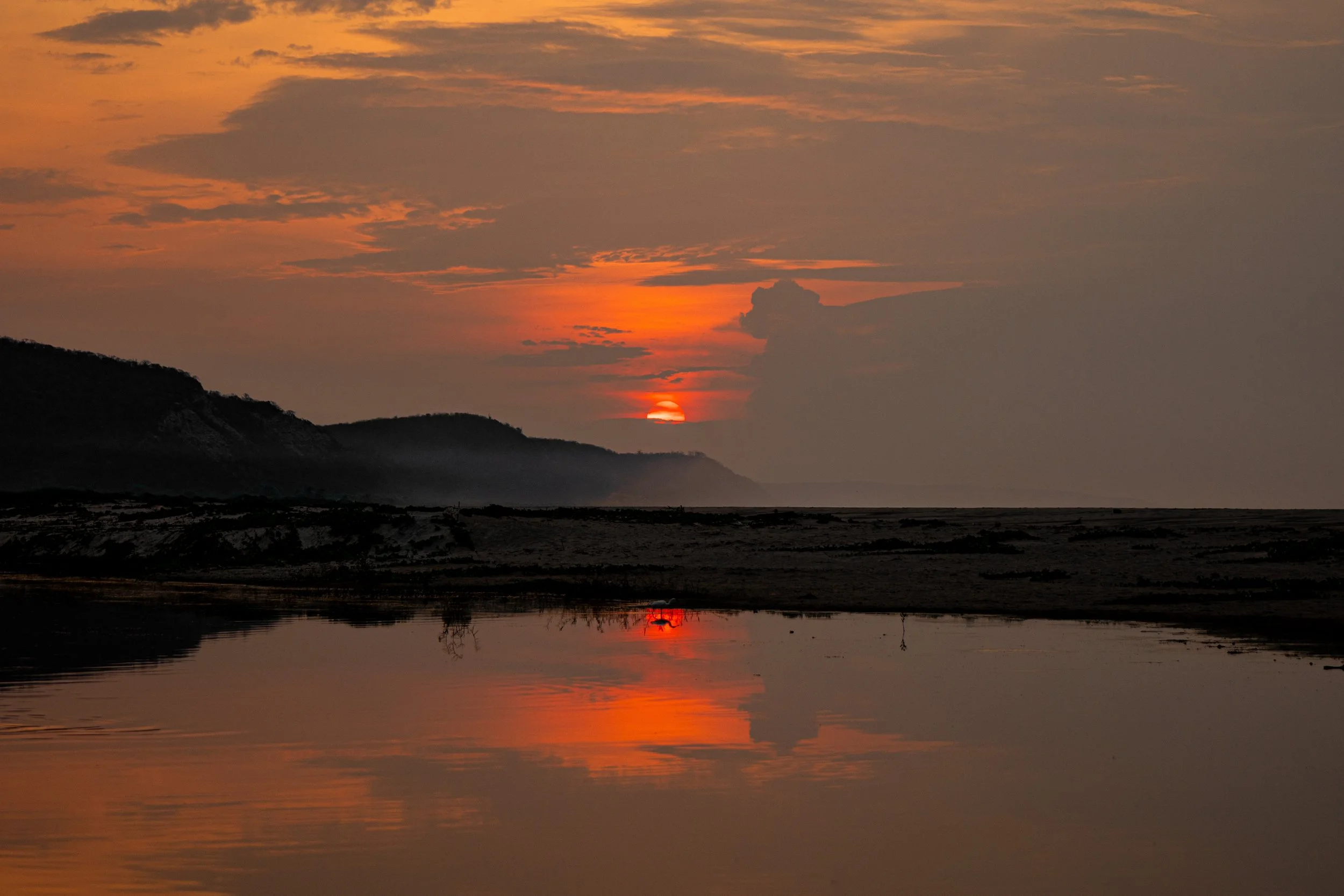 Sunset over a body of water with mountains in the background and a reflection of the sky on the water.