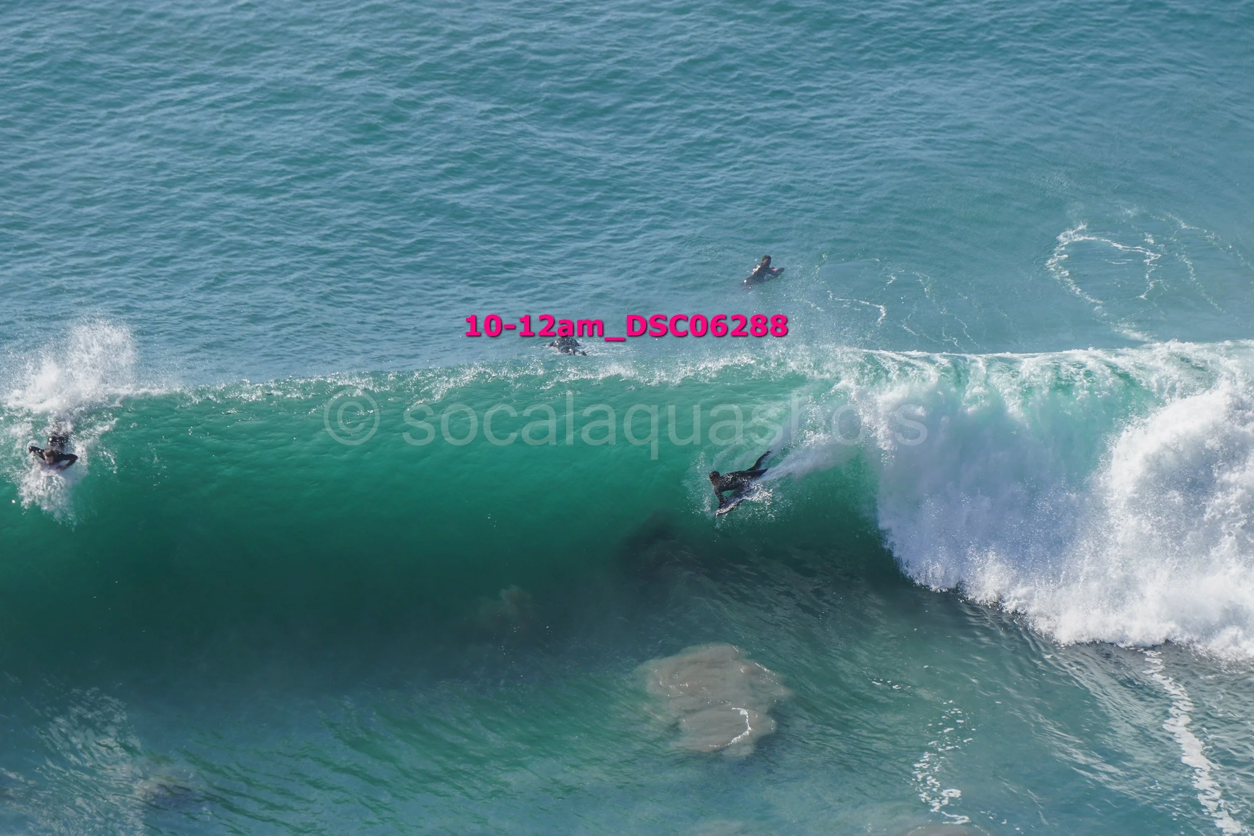 Group of surfers riding a large ocean wave with some surfers in the background and others falling off the wave.