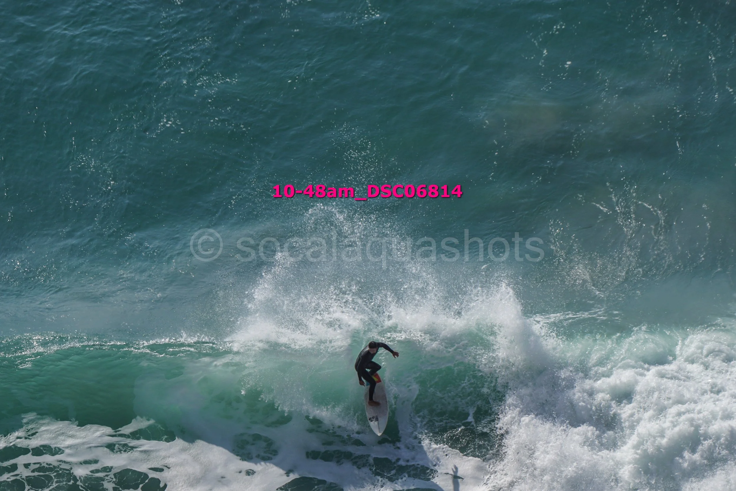 A person surfing on a wave in the ocean, wearing dark clothing and balancing on a surfboard.