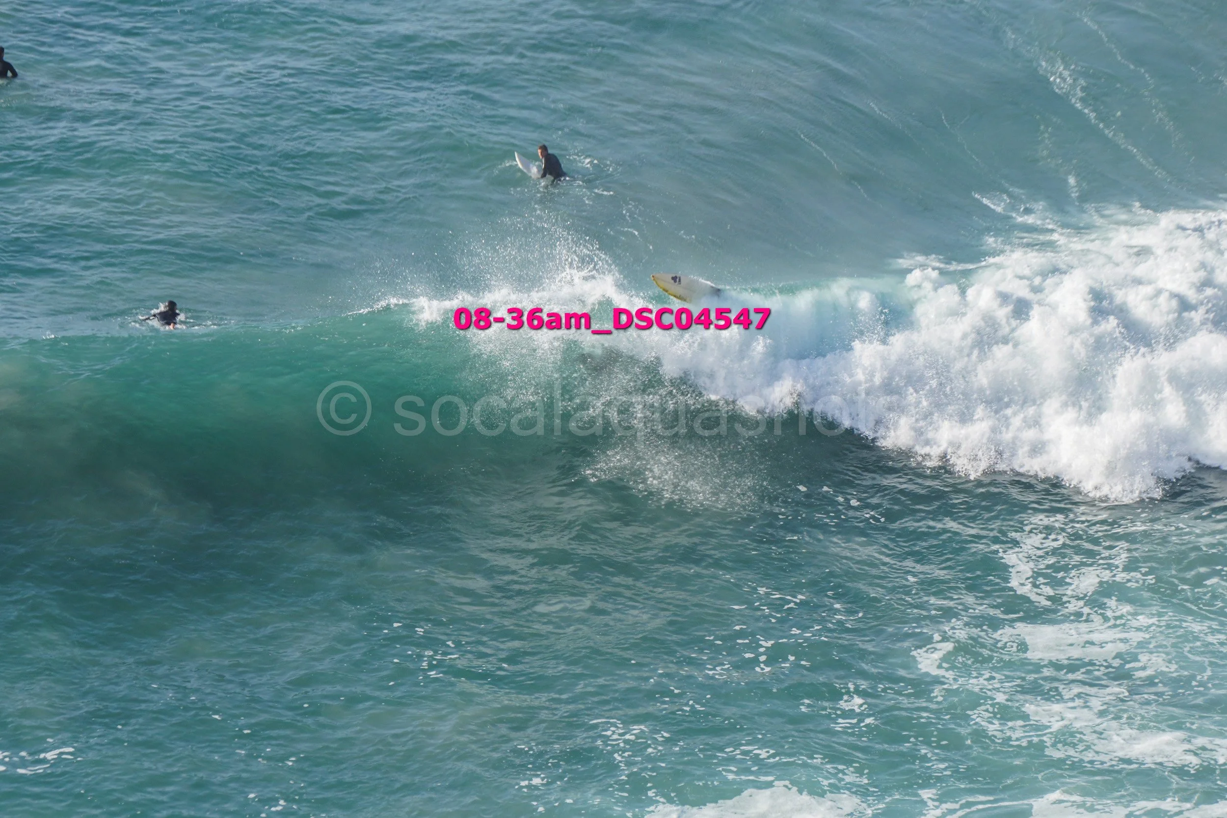 Surfboarder riding a wave with two surfers in the water nearby.