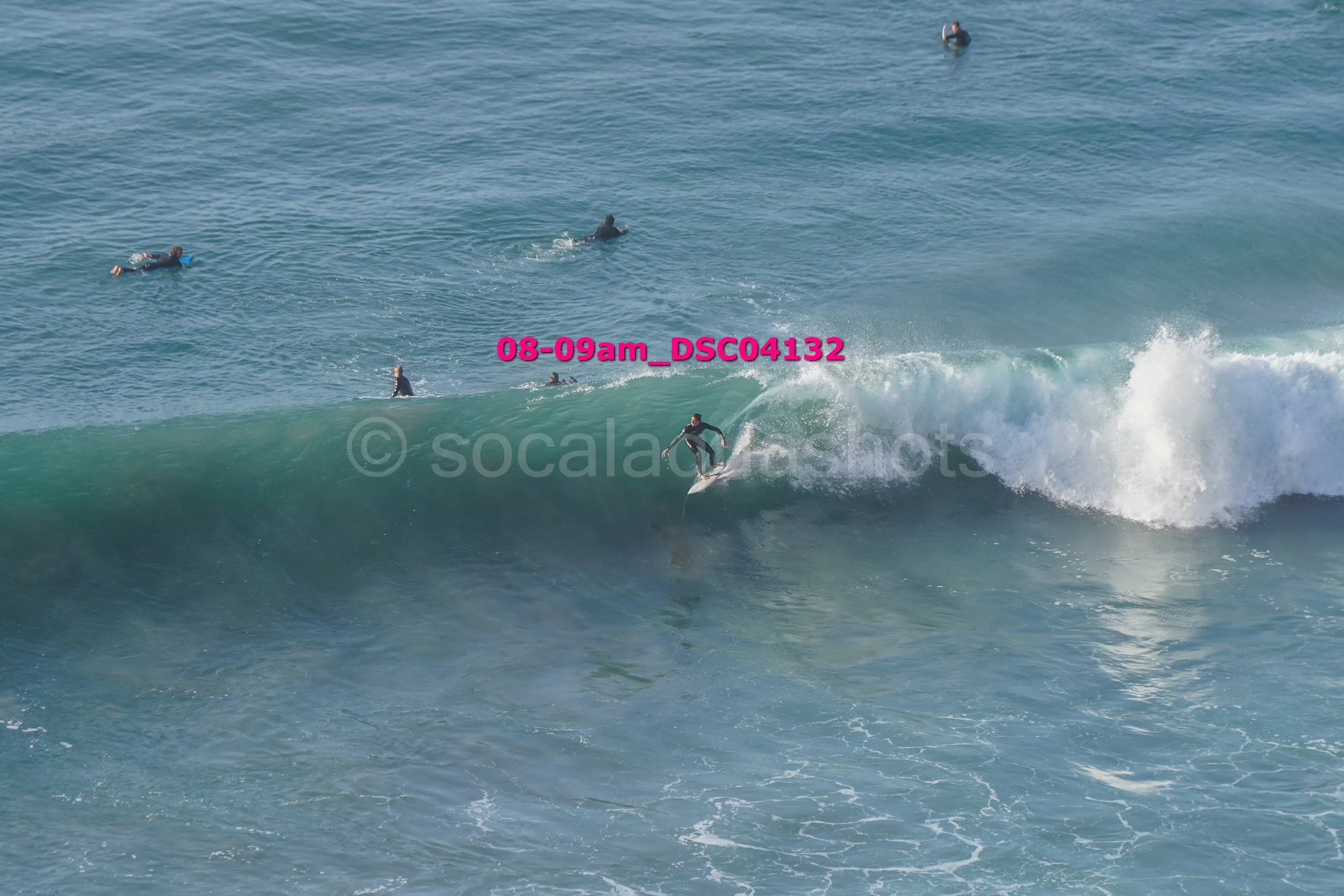 Surfer riding a wave with several people in the water watching from a distance.