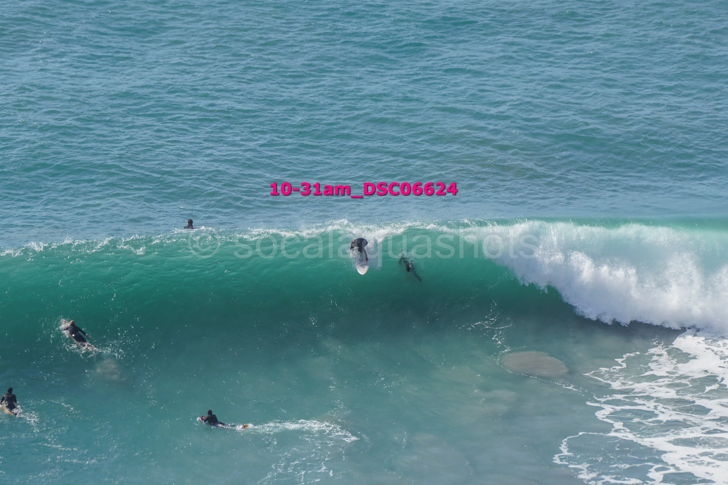 Several surfers riding a large wave in the ocean with one person paddling in the water nearby.