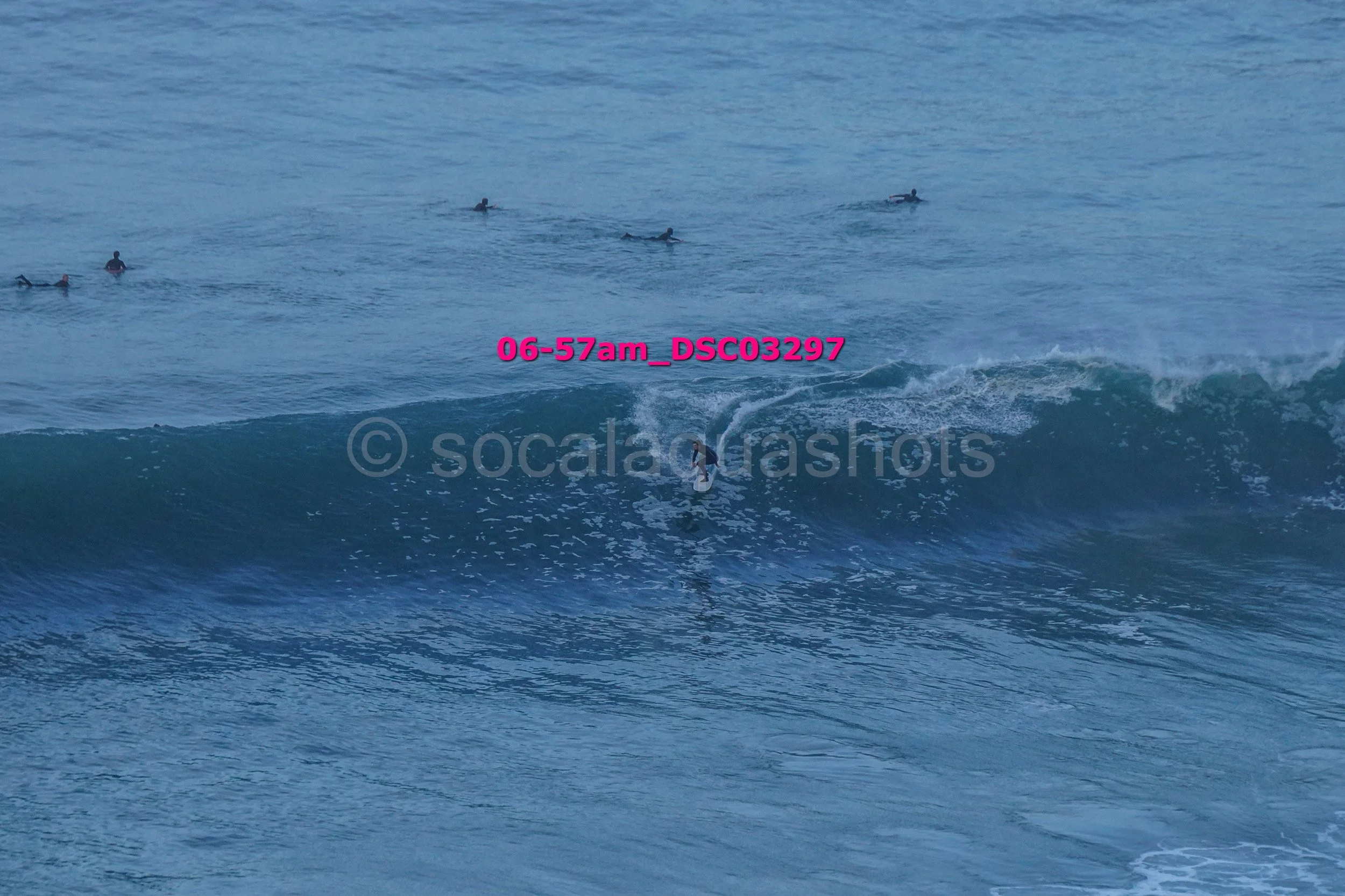 Surfer riding a wave in the ocean with several surfers in the background.