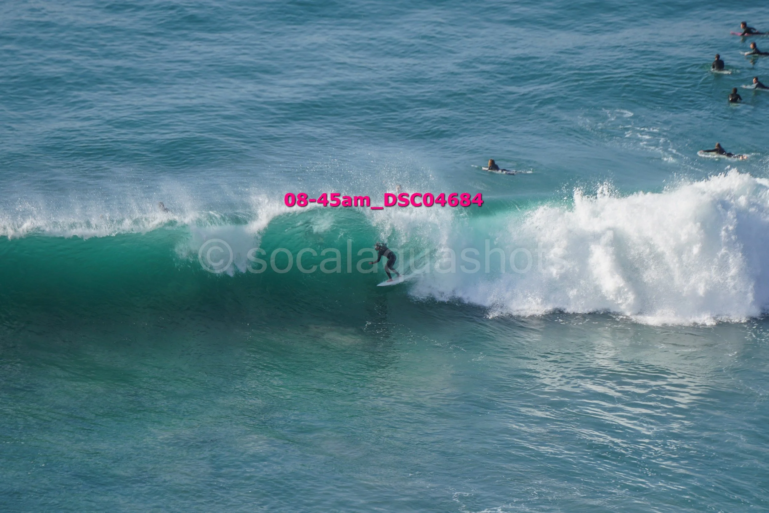 Surfer riding a wave with multiple surfers in the water nearby.