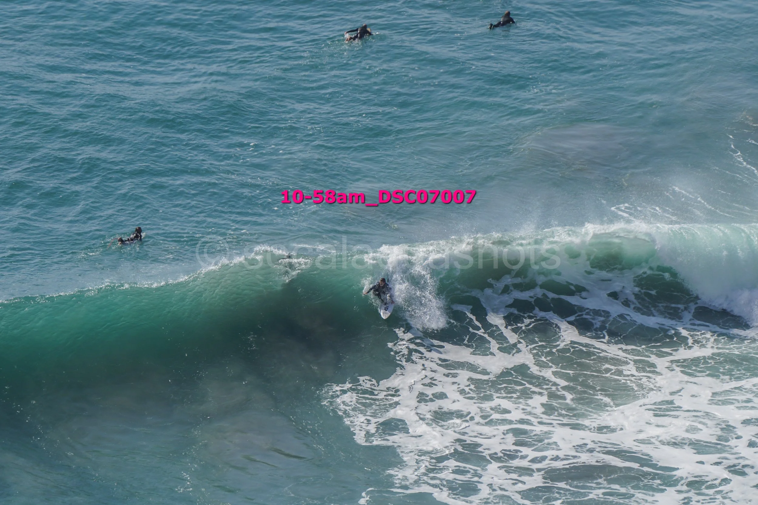 Surfer riding a wave with multiple surfers in water nearby, with some paddling and others observing.