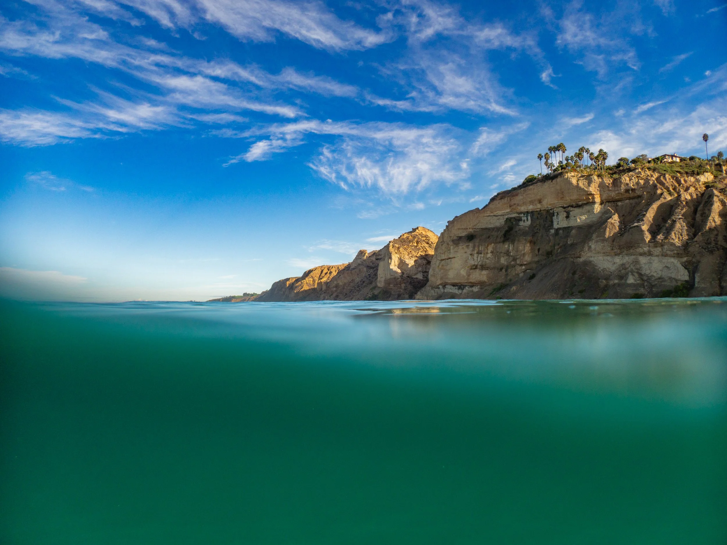 View of ocean and cliffs with palm trees under blue sky with clouds