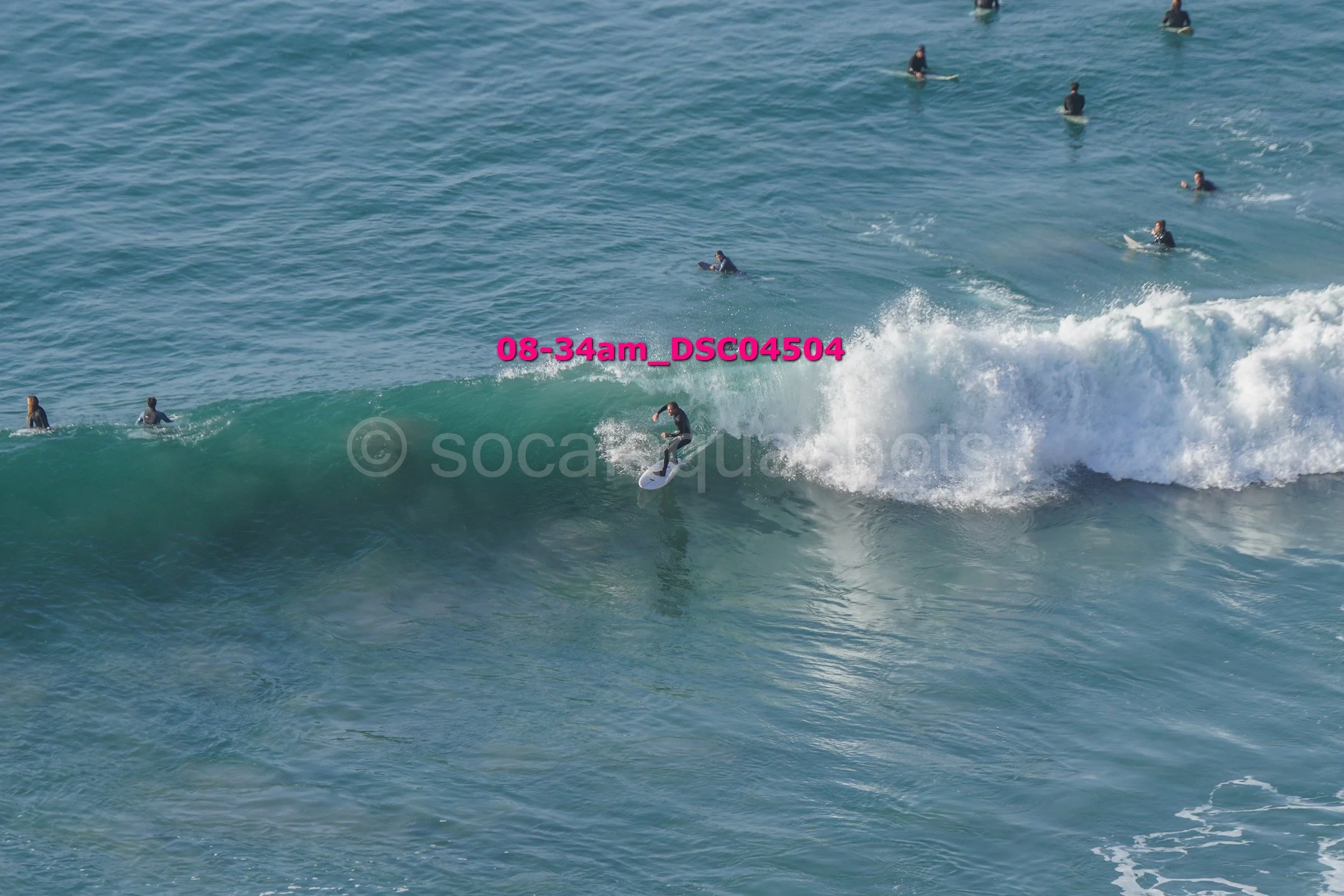 A person surfing on a wave with several people swimming and surfing in the ocean in the background.