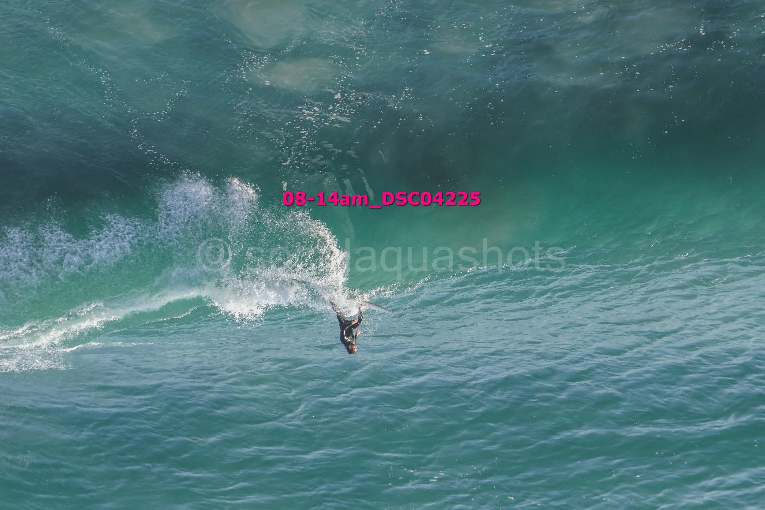 A person surfing on a wave in the ocean, with spray of water and a large wave behind them.