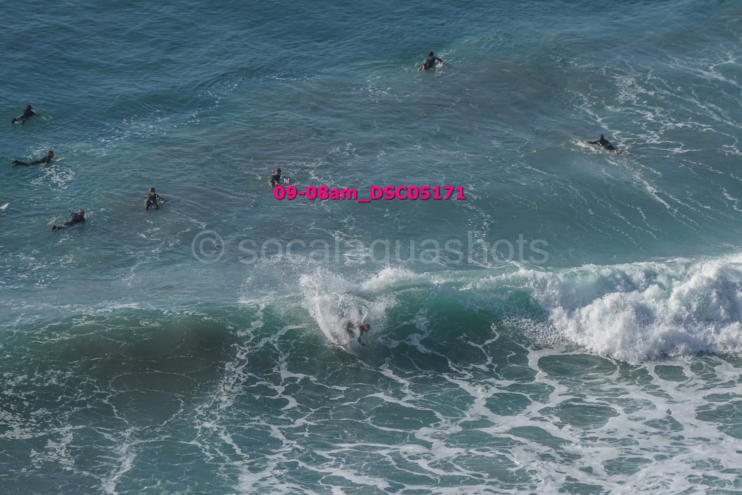 Surfer riding a wave with others swimming in the background at the ocean.