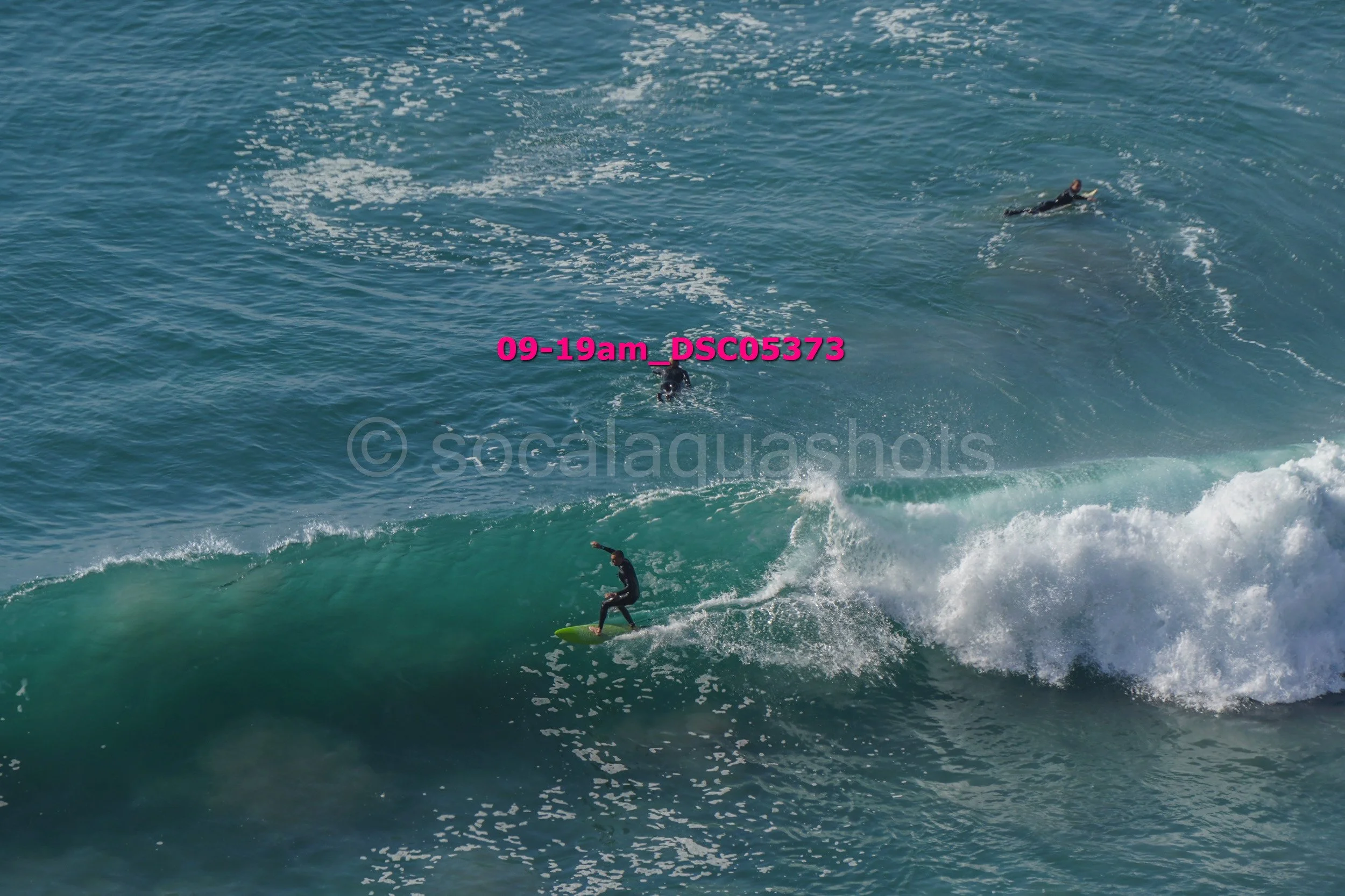 A person surfing on a wave with two other surfers in the water nearby.