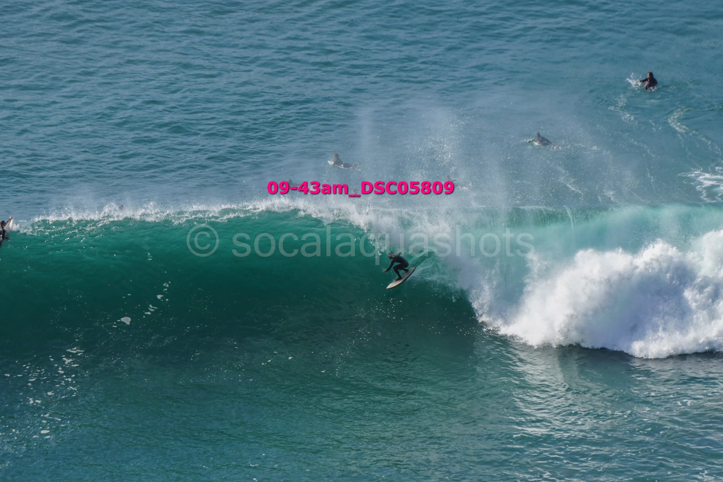 A person surfing on a large wave in the ocean with other surfers in the background.