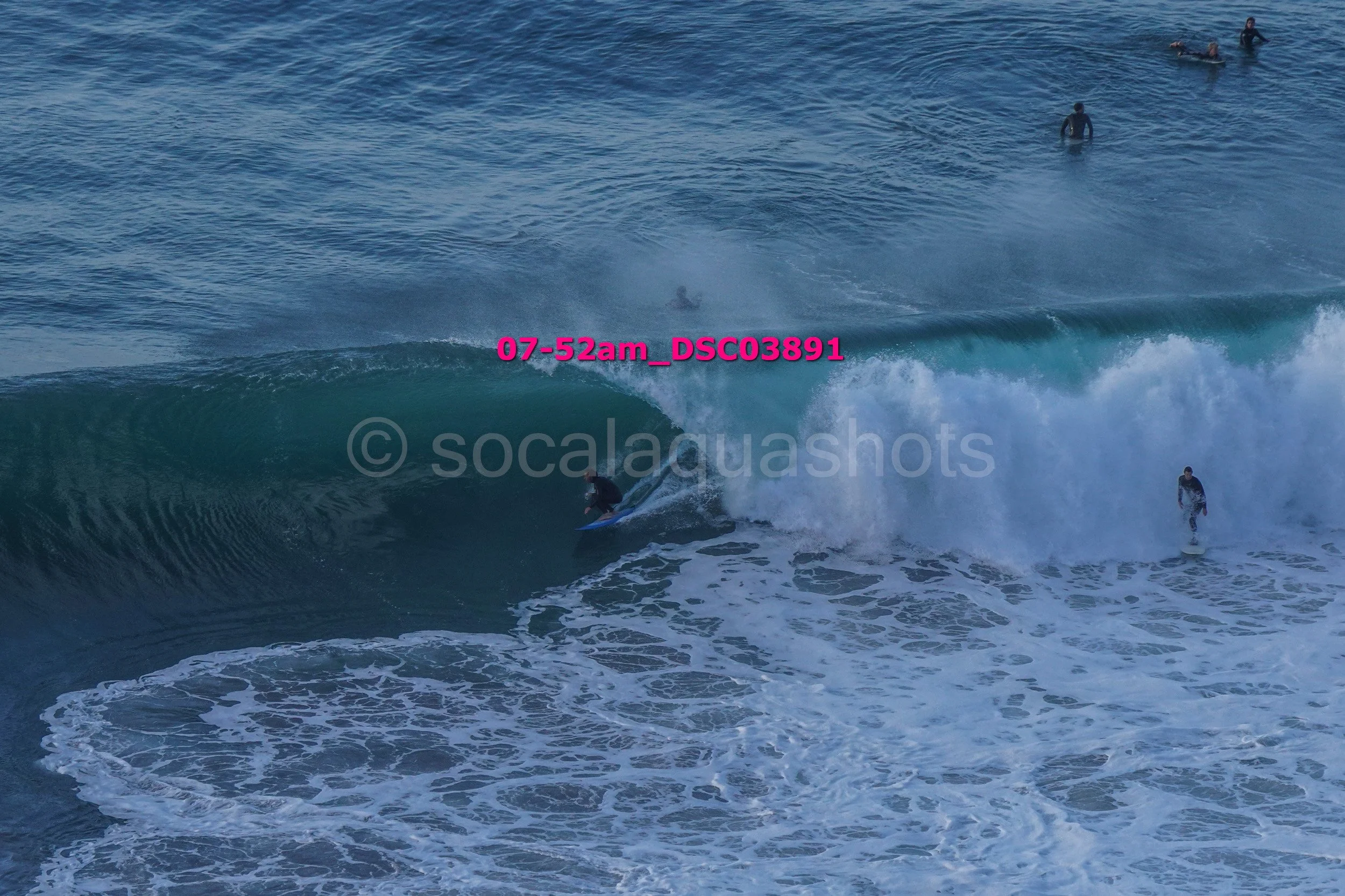 Surfer riding a large wave with several people in the water in the background.