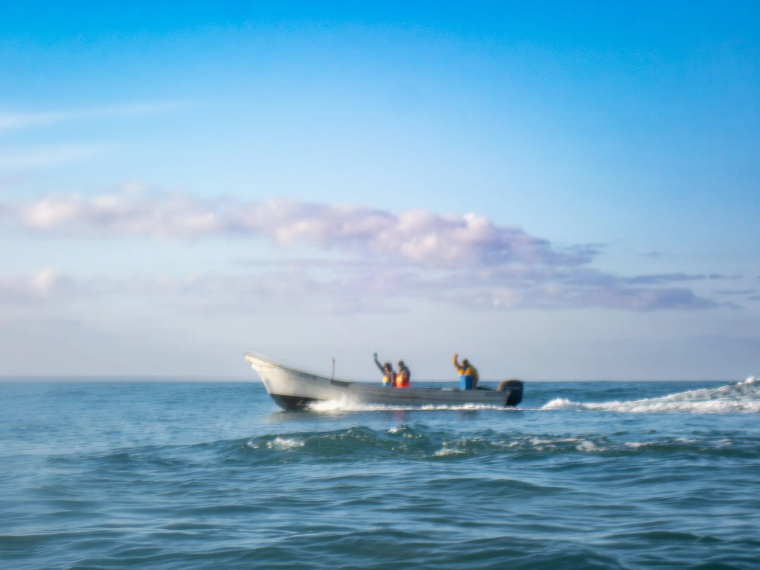 A boat with four people on it navigating through ocean waves under a partly cloudy sky.