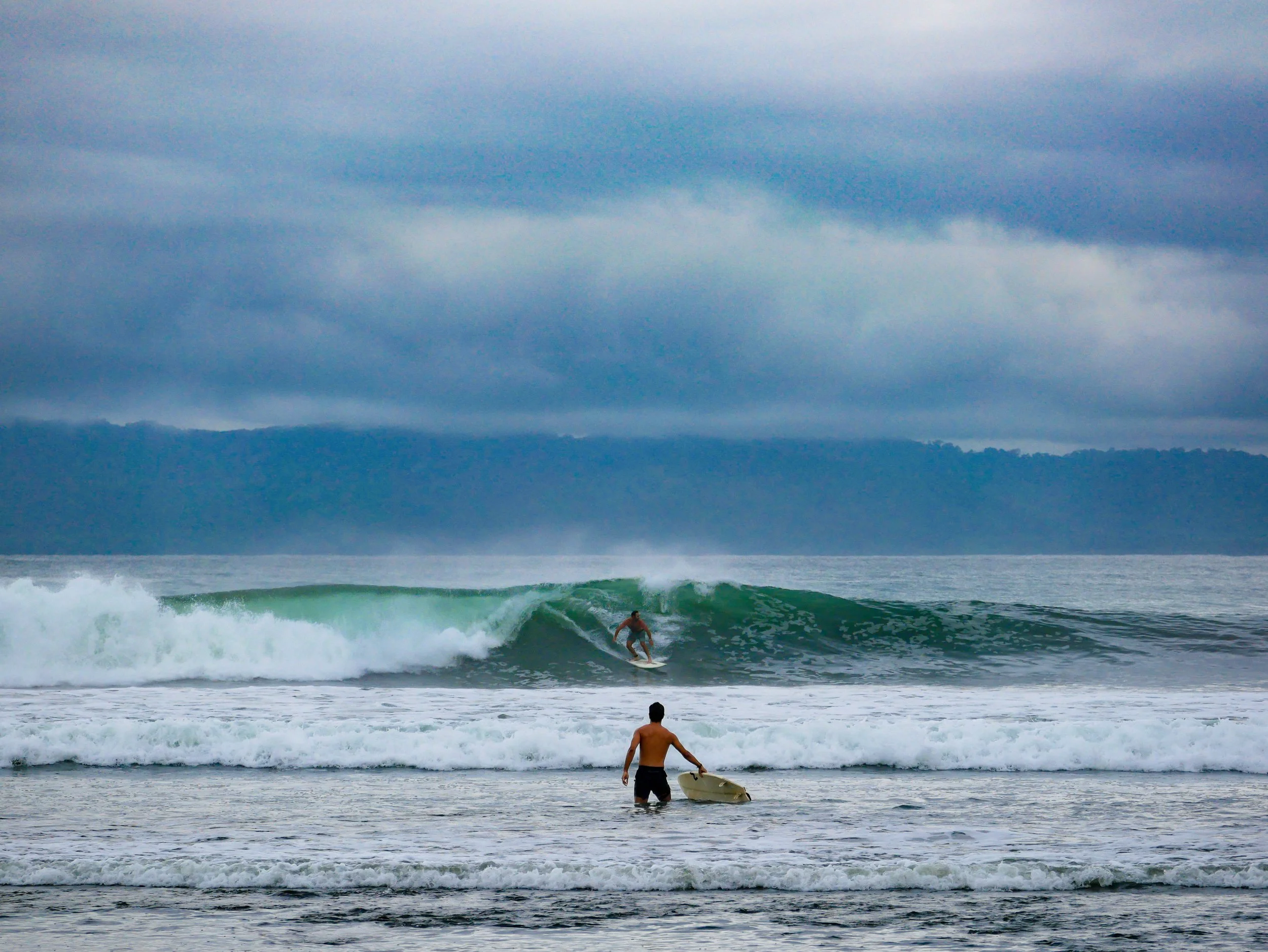 Surfers at a cloudy beach with waves