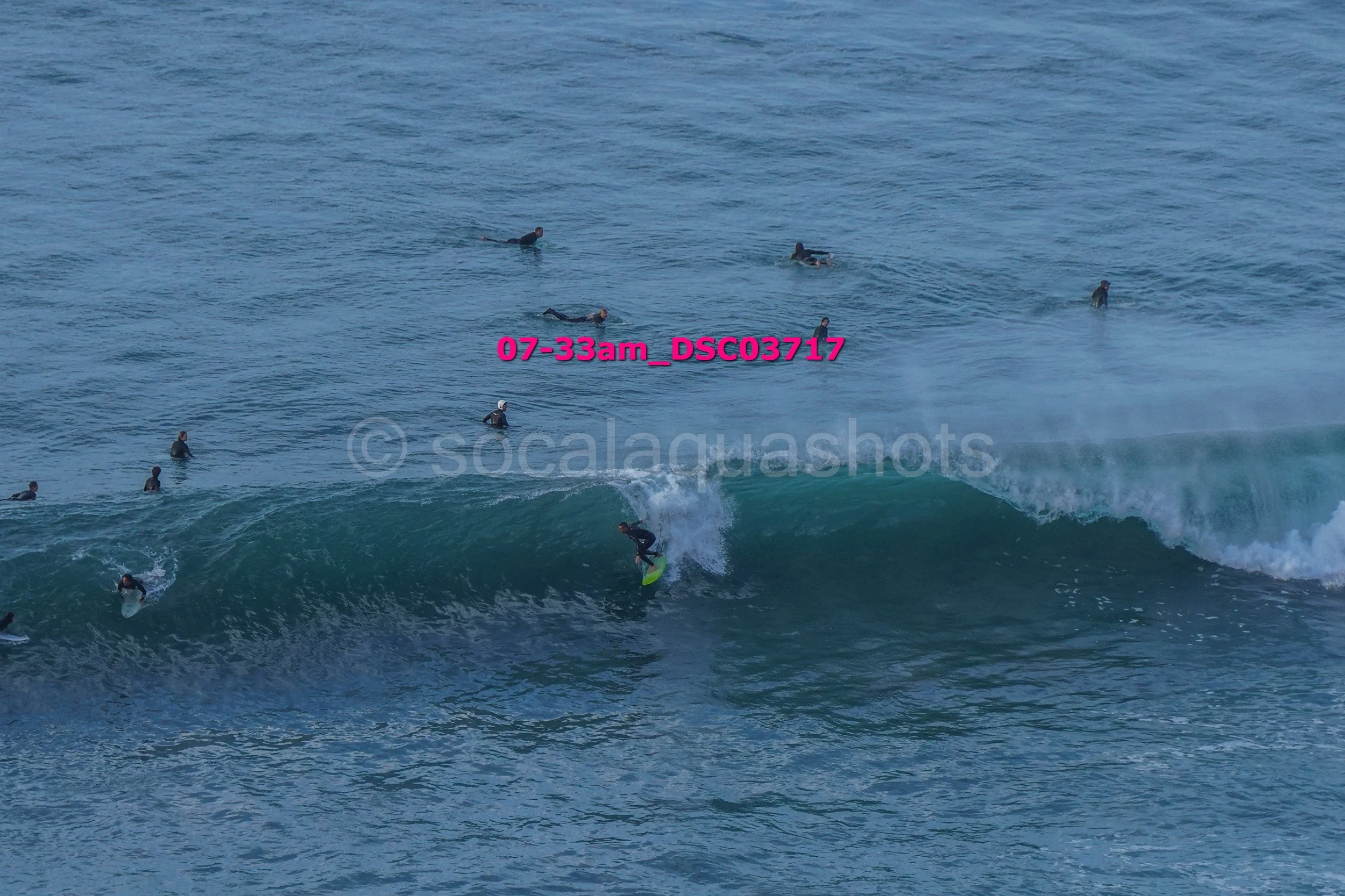 Surfer riding a wave with multiple surfers in the water around him in the ocean.