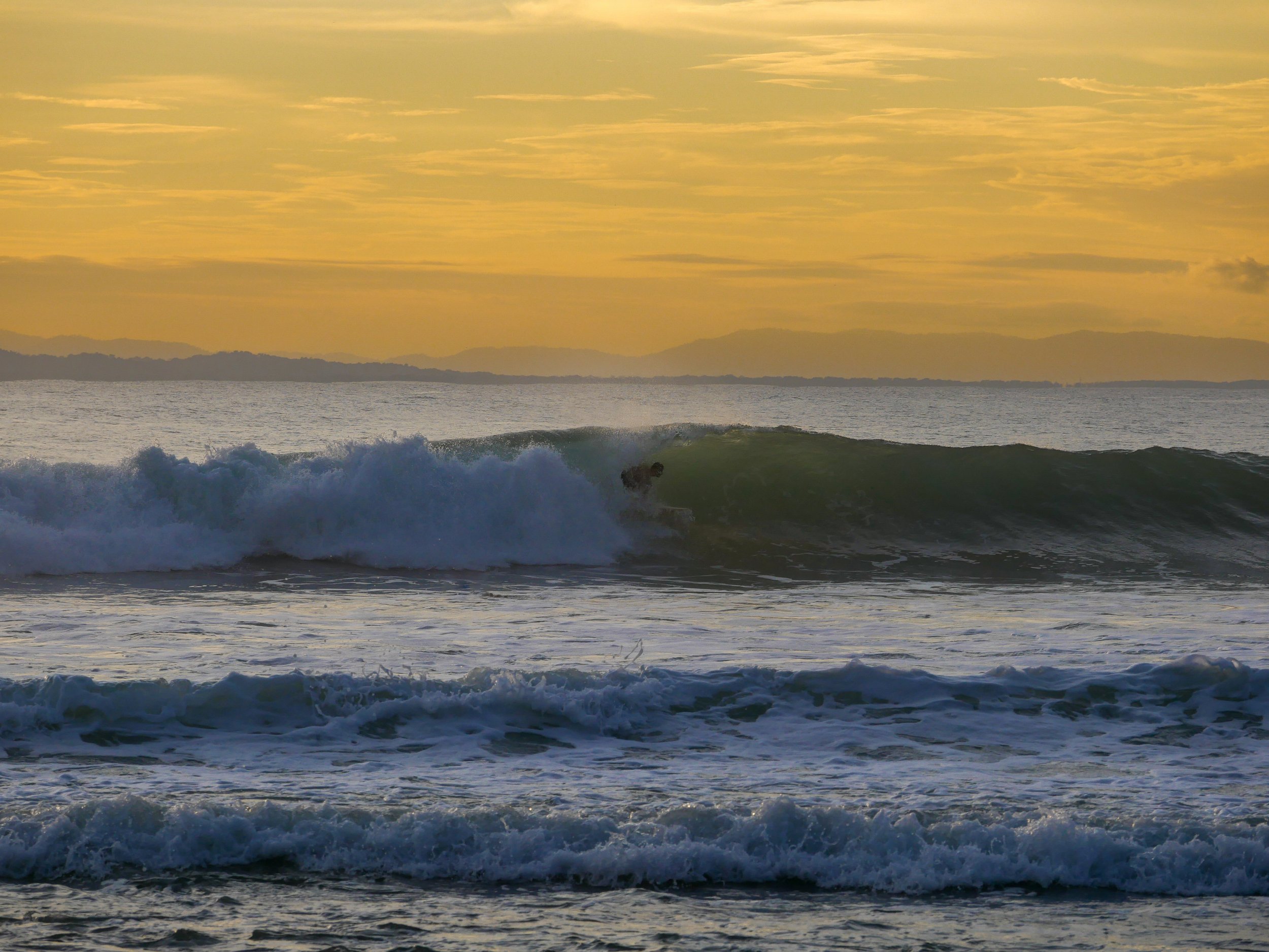 Surfer riding a wave at sunset in ocean