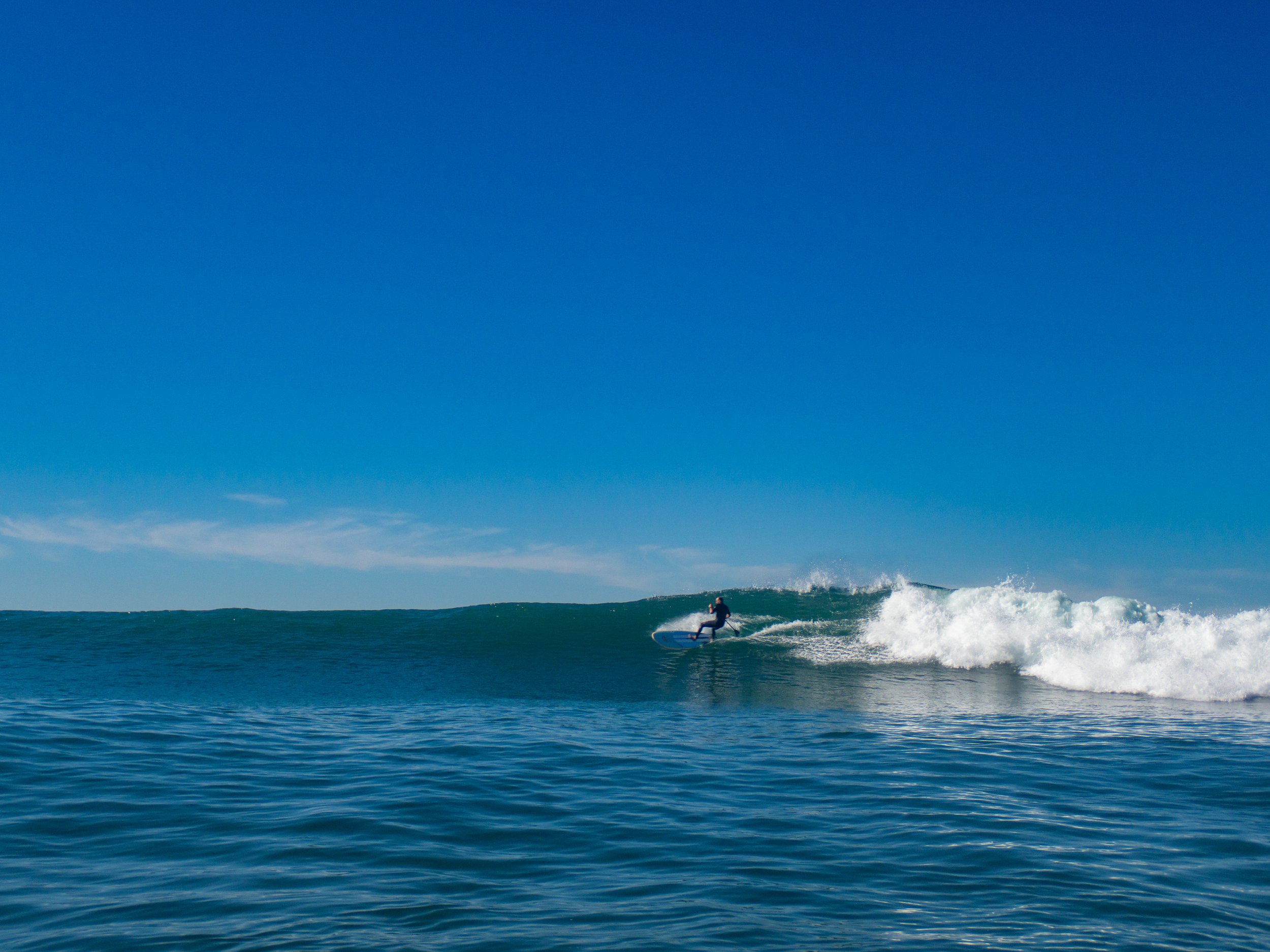 A person surfing on a wave in the ocean under a clear blue sky.