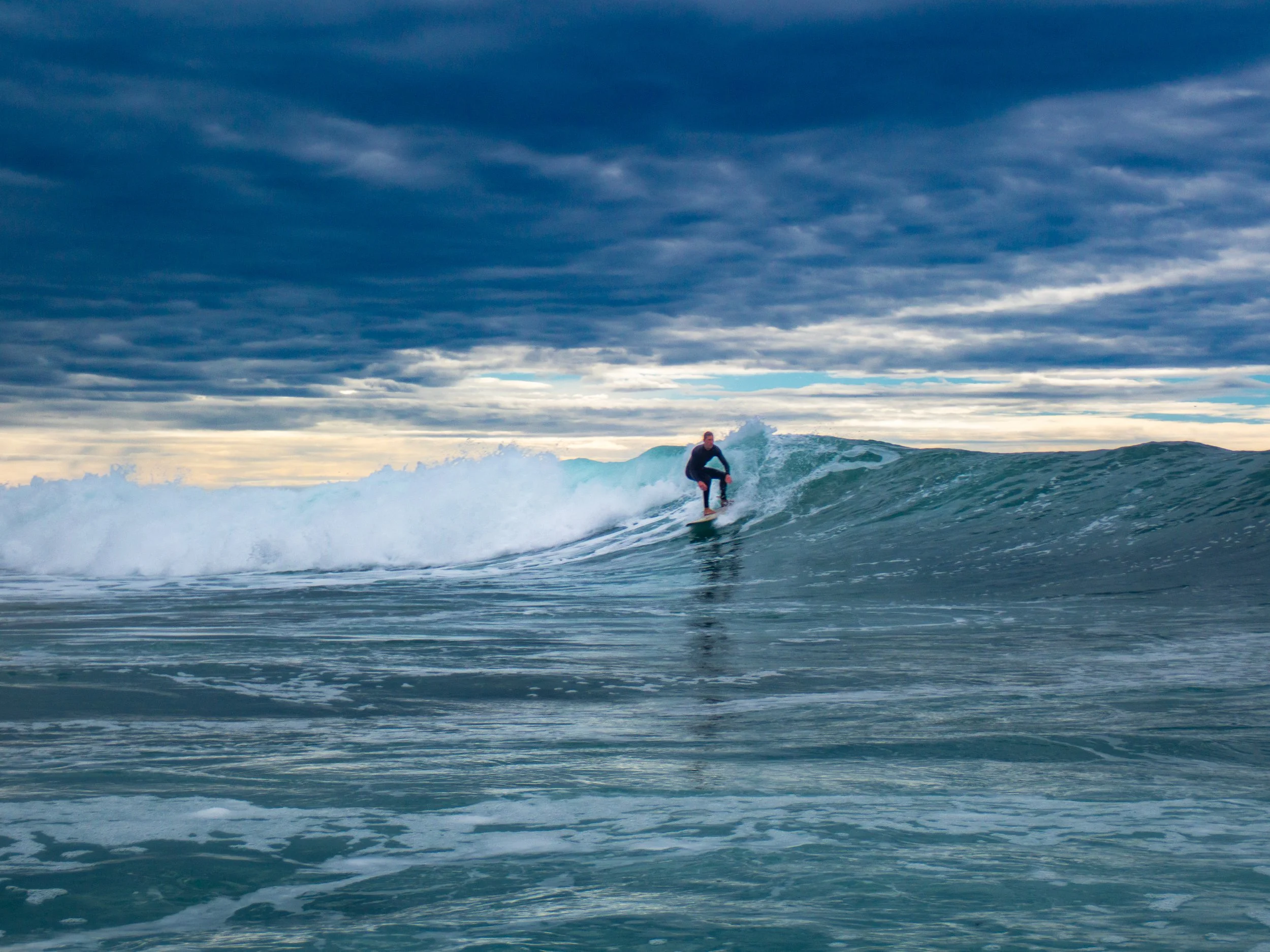 Person surfing on a wave in the ocean during cloudy weather.