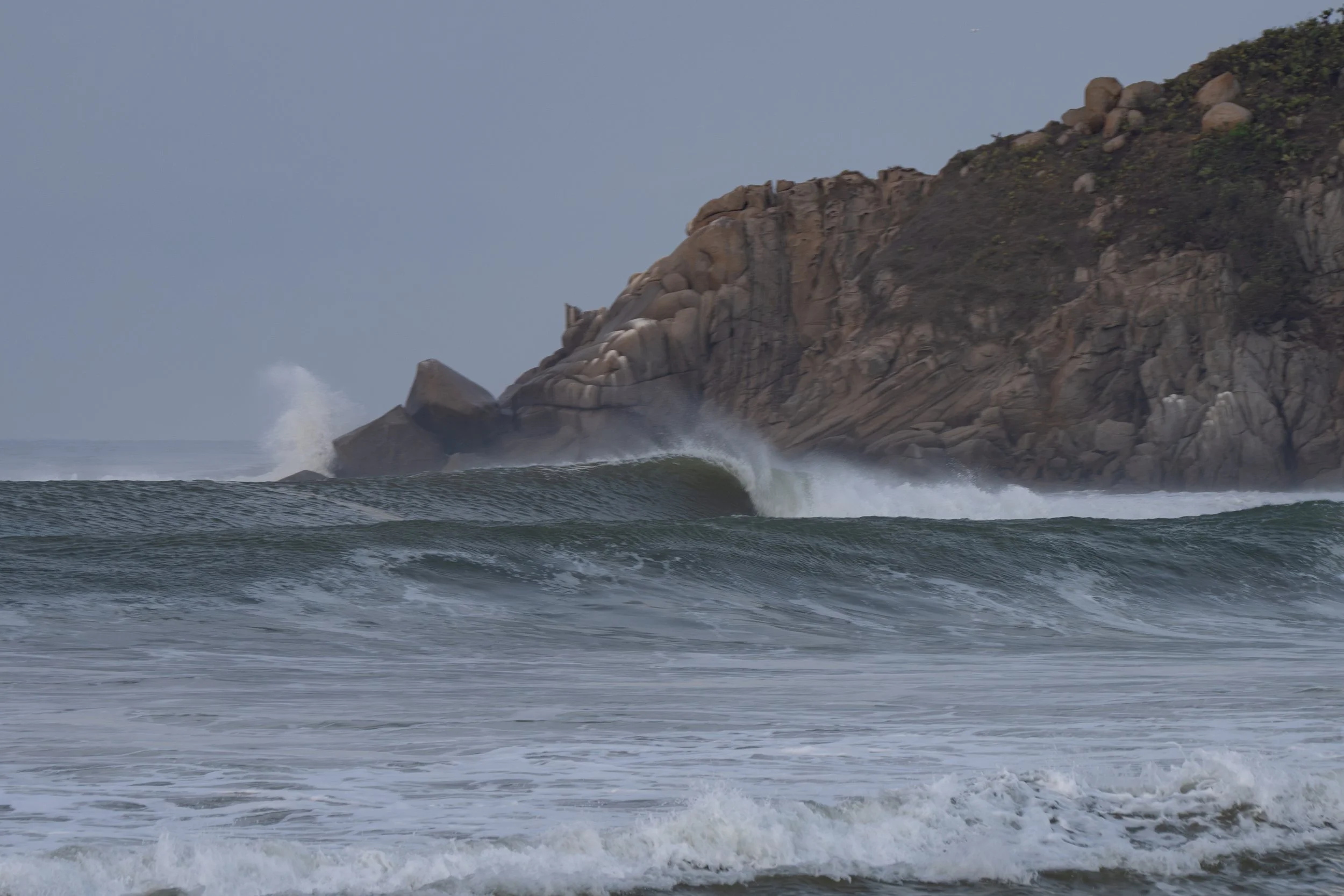 A rocky cliff with waves crashing against the rocks in the ocean.