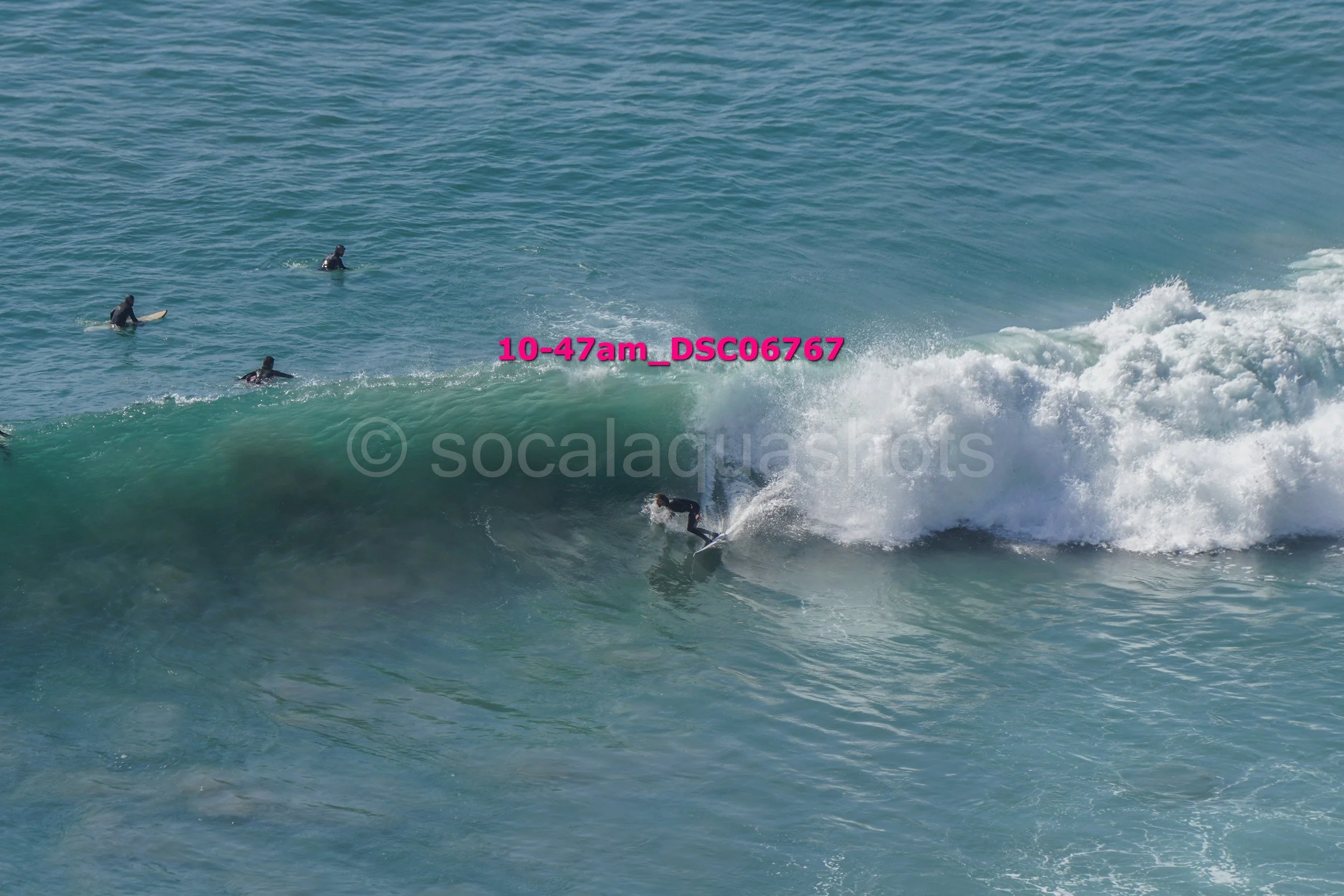Surfer riding a large wave with four surfers in the water in the background at the beach.