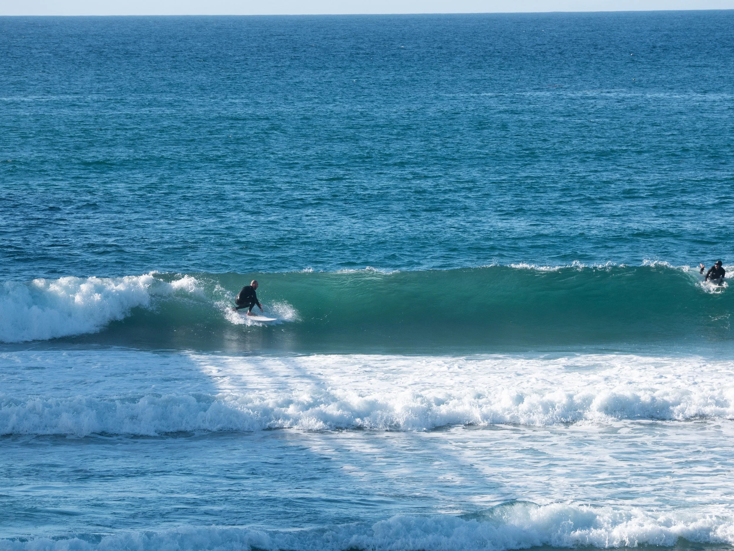 A person surfing on a wave in the ocean with two other surfers in the background.