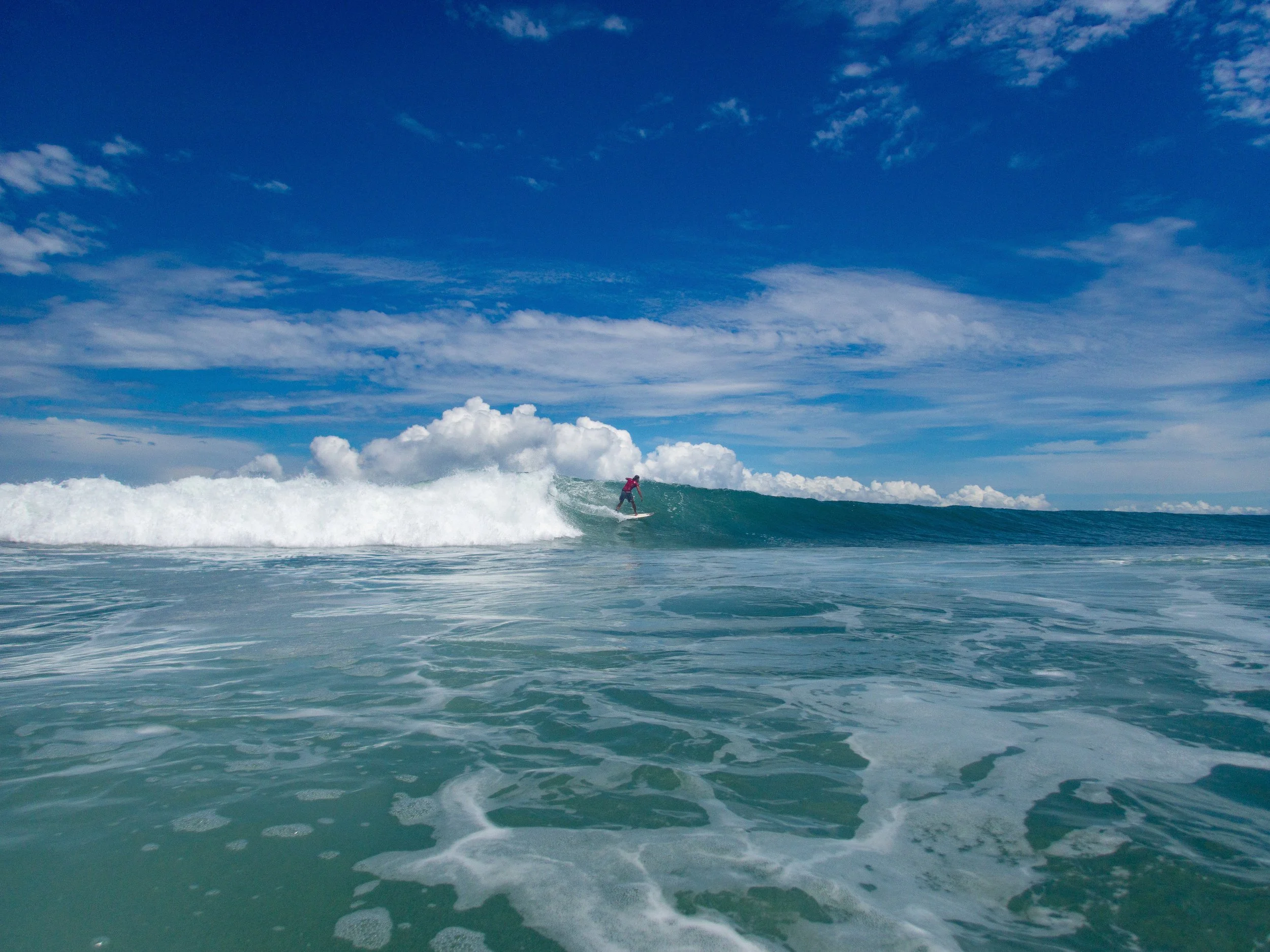 Surfer riding a wave under a blue sky with clouds