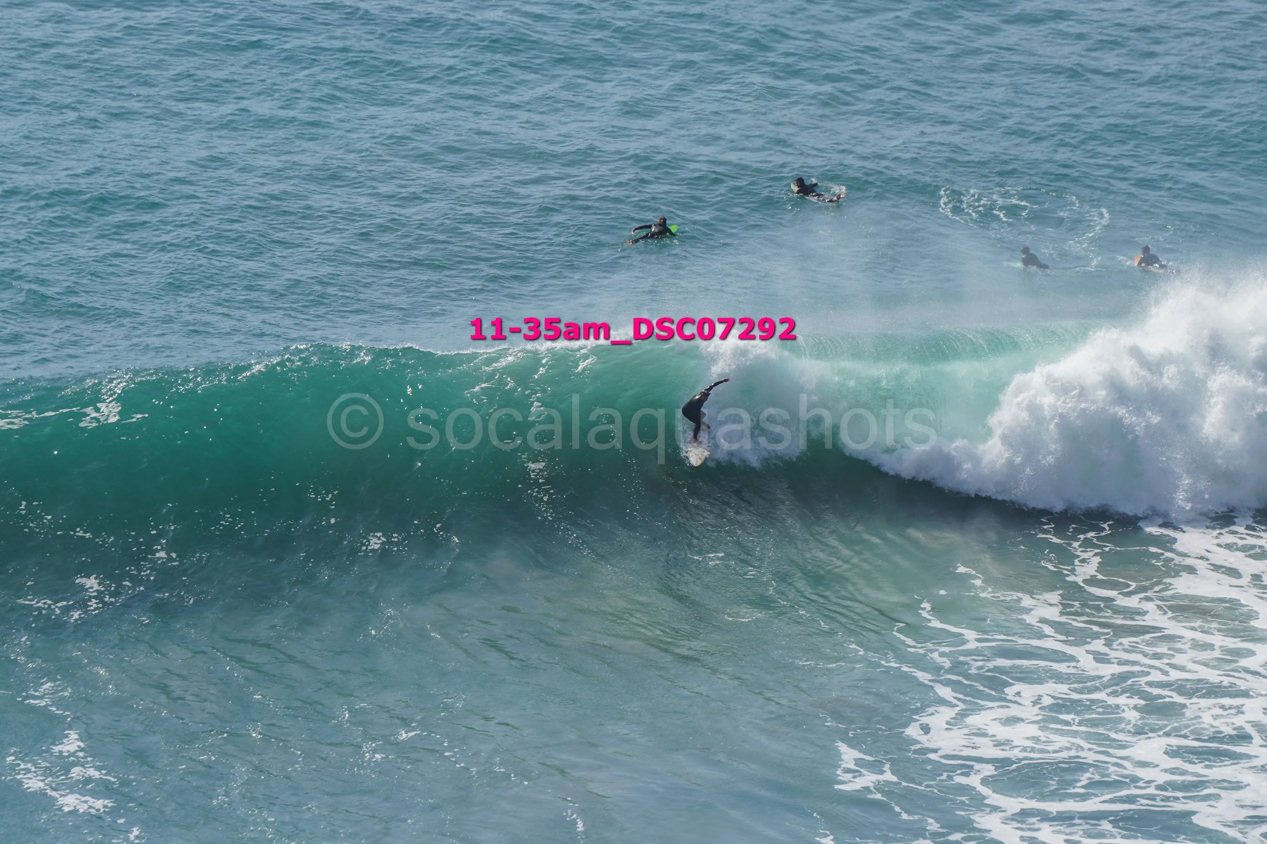 Surfer riding a wave with four other surfers in the water behind, during daytime