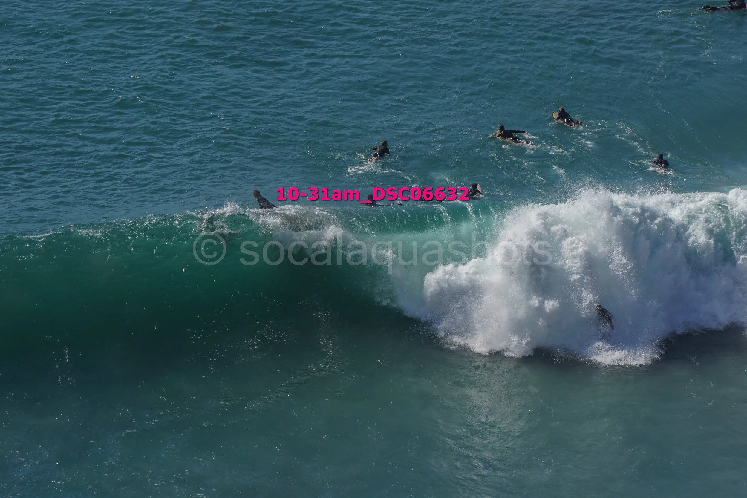 Group of surfers in wetsuits riding a large wave in the ocean.