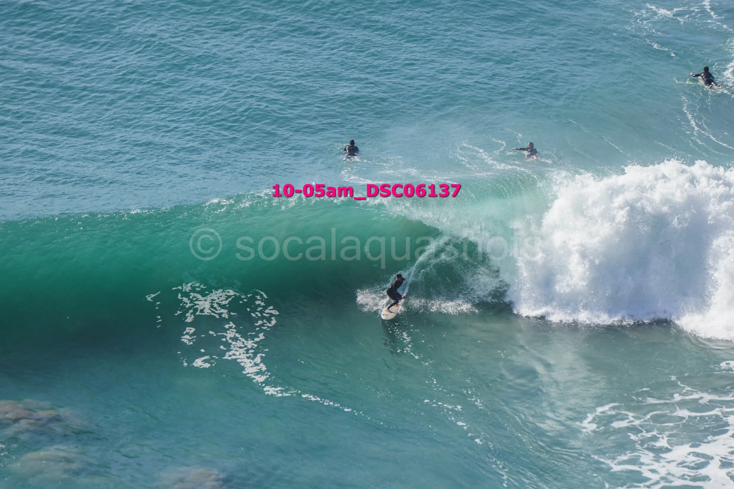 Surfer riding a large wave with three people in the water watching from further out.