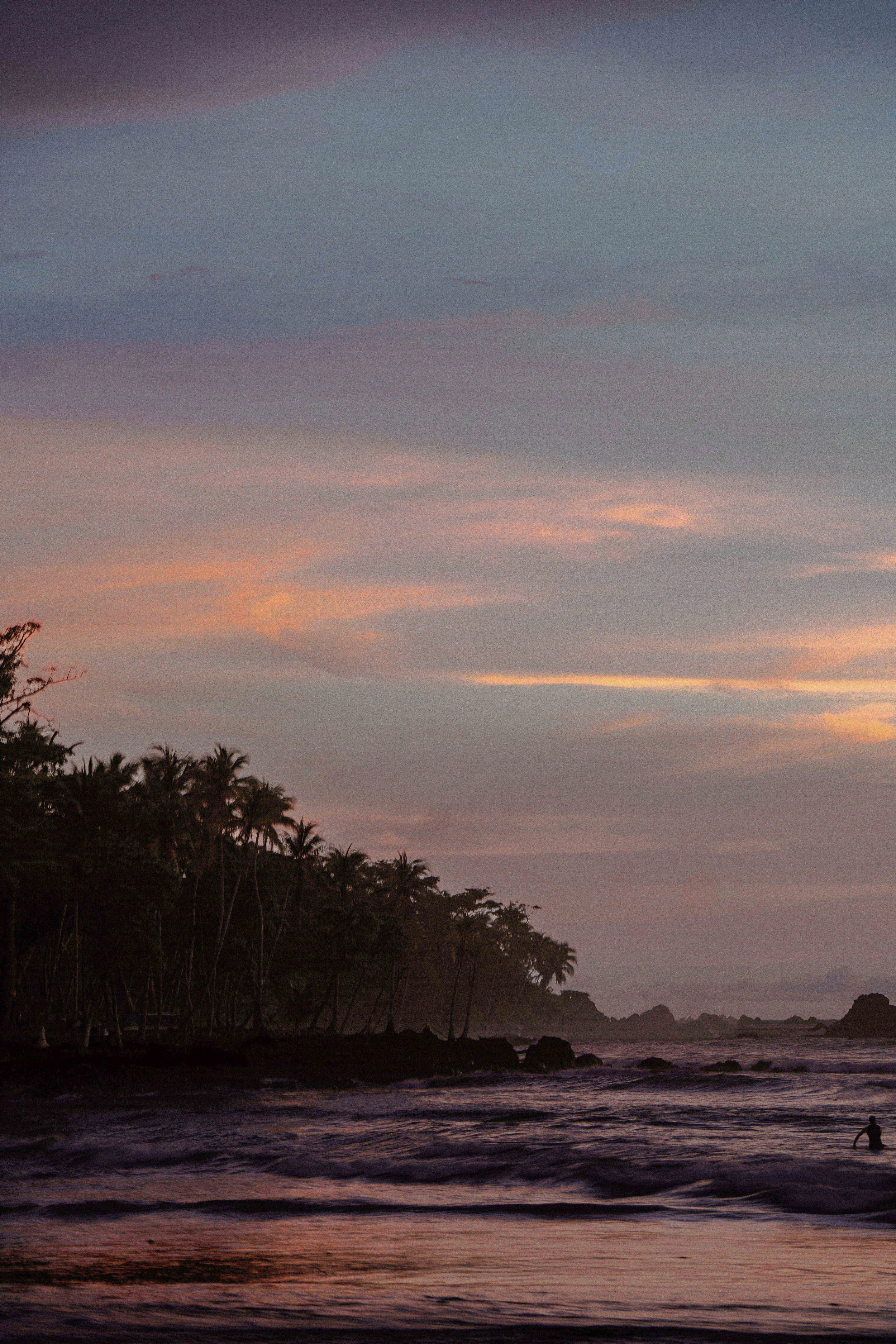 Sunset over a tropical beach with palm trees along the shoreline and waves crashing on the sand.