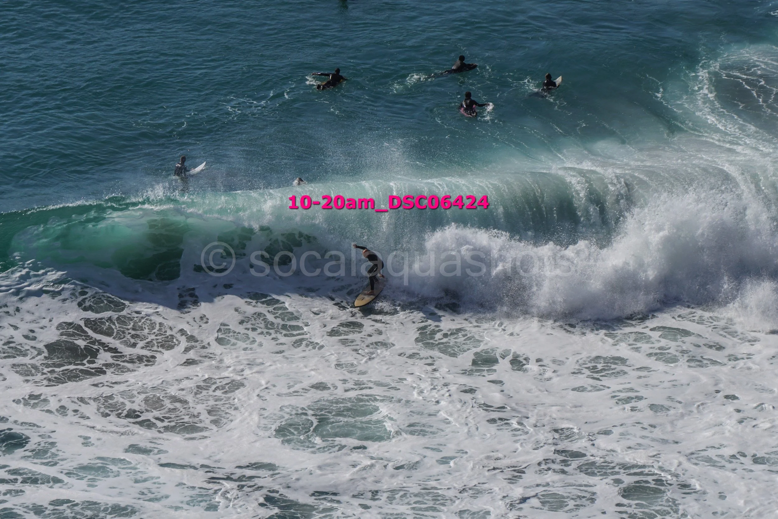 A surfer riding a wave with multiple people in the water in the background.