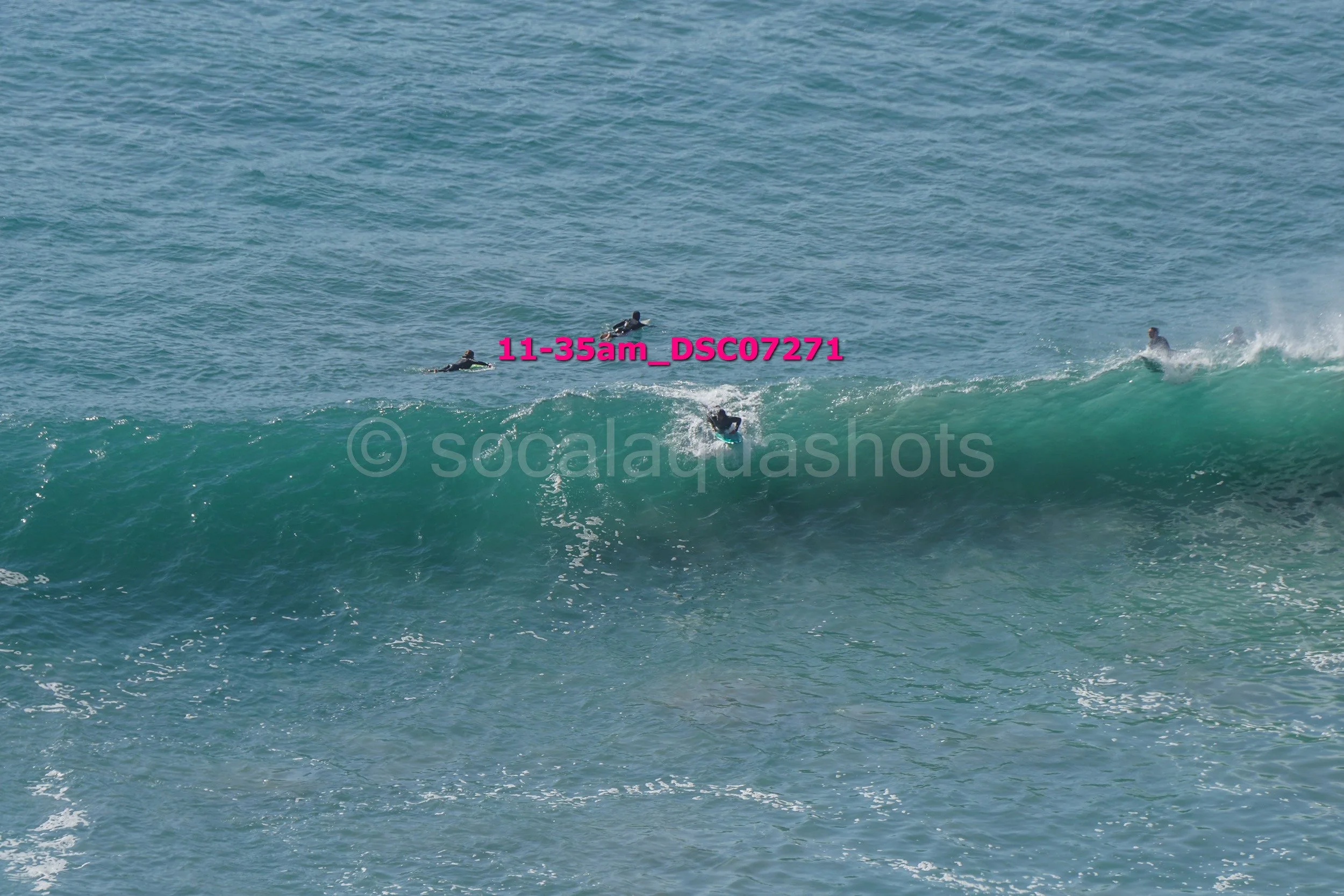 People surfing on a large ocean wave with multiple surfers in the water.