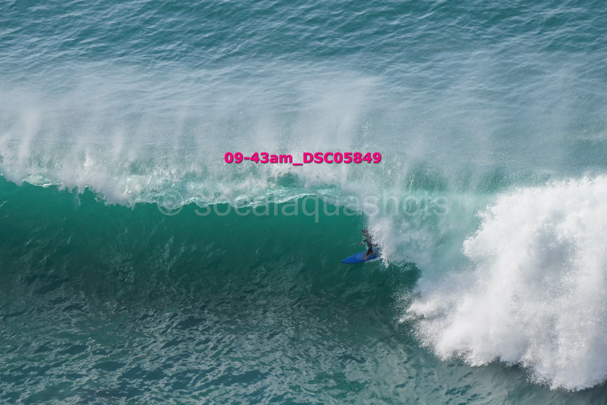 A person surfing on a large ocean wave with white foam and spray.