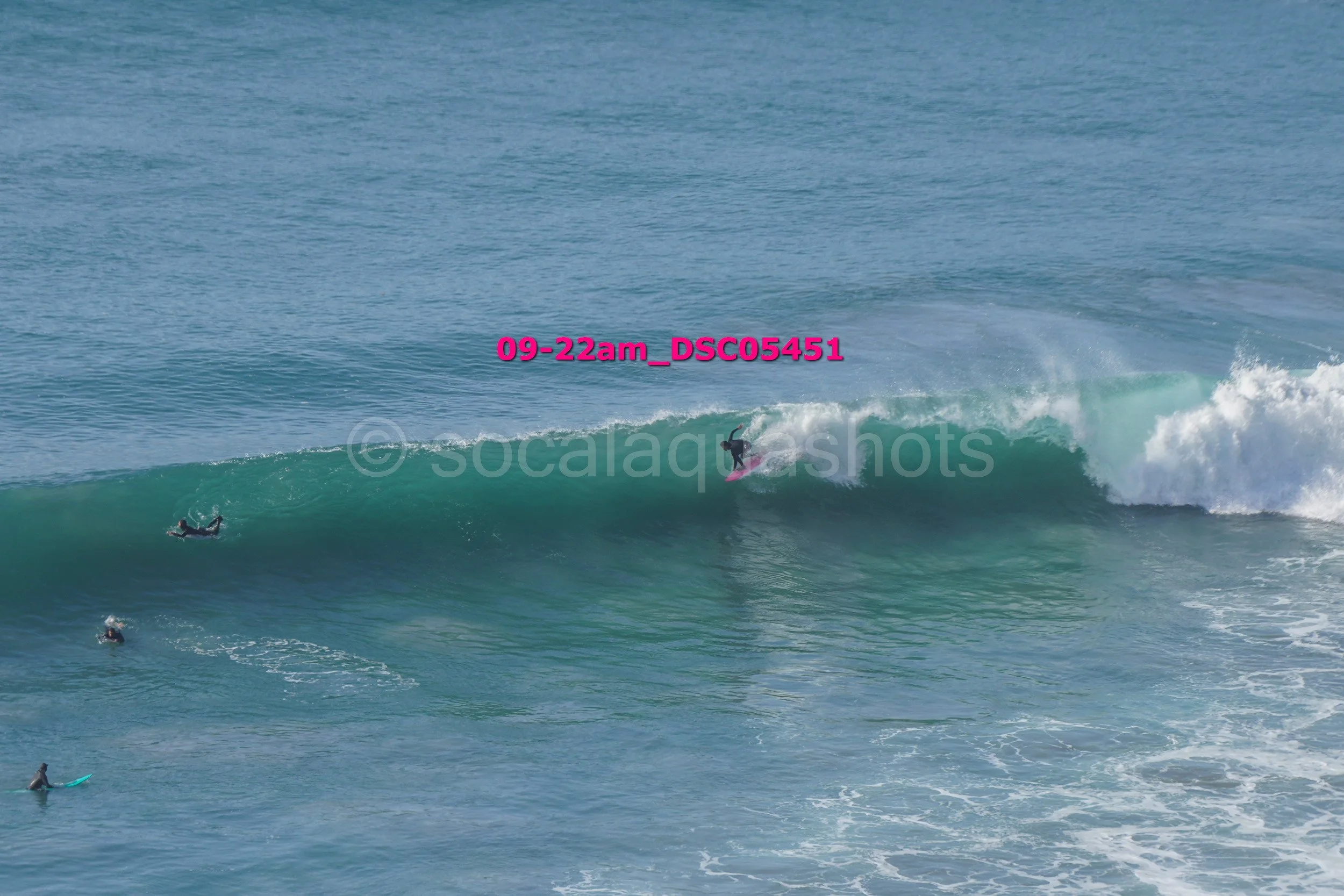 Surfer riding a large wave in the ocean with others surfing nearby.