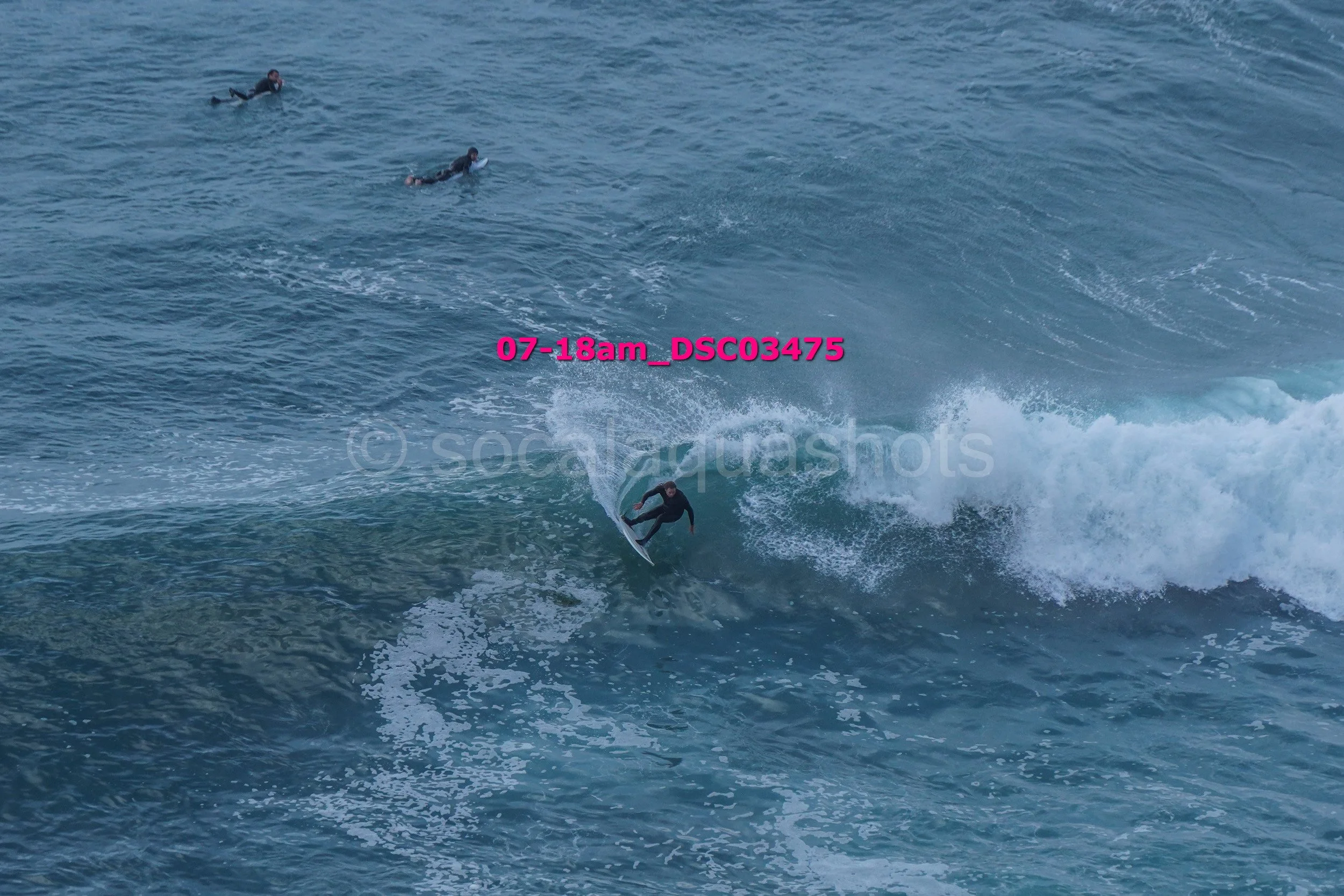 A person surfing a wave with three surfers in the distance in the water.