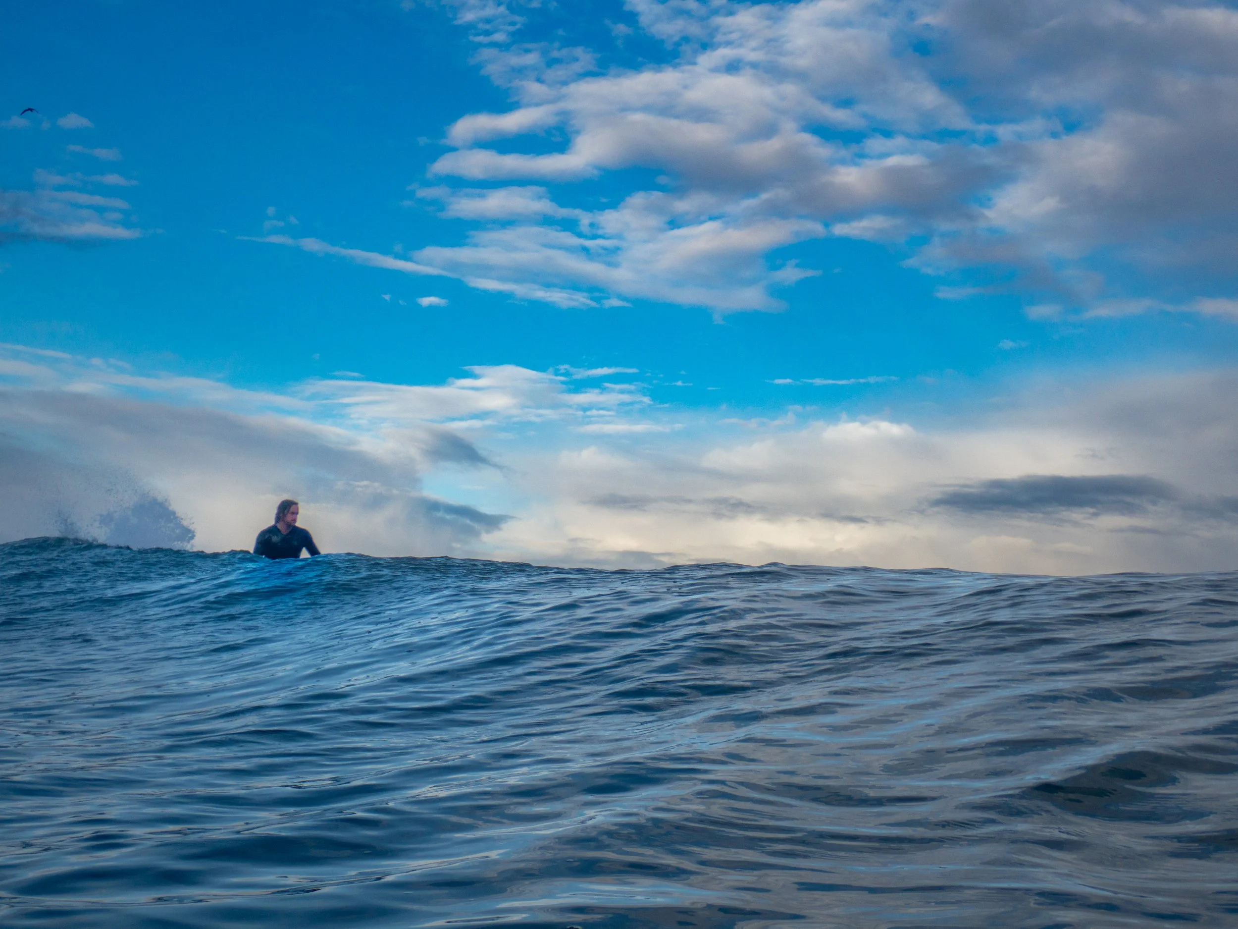Person sitting on a surfboard in the ocean with a partly cloudy sky in the background